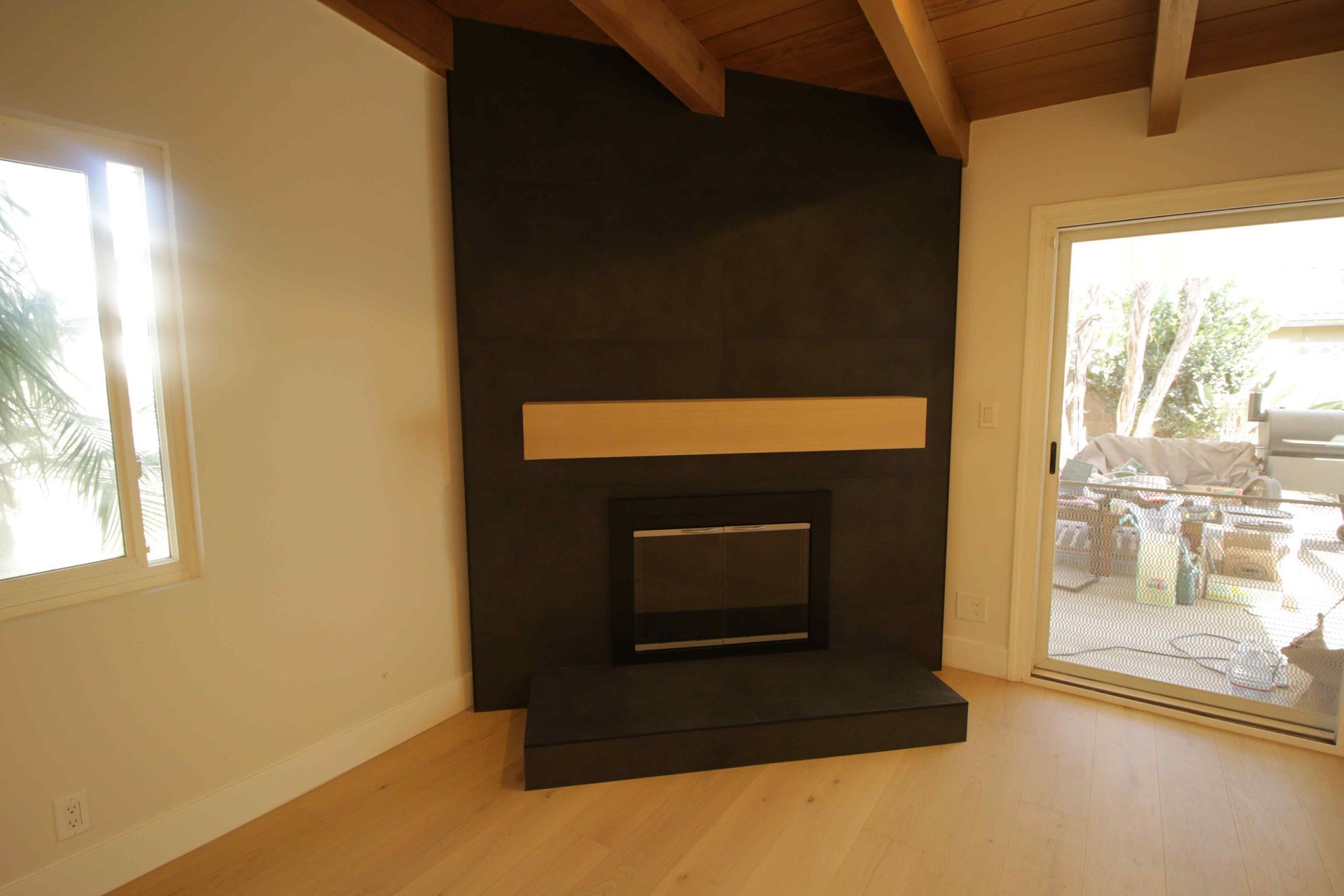 Modern living room with a black fireplace, beige walls, wood ceiling, and large windows.