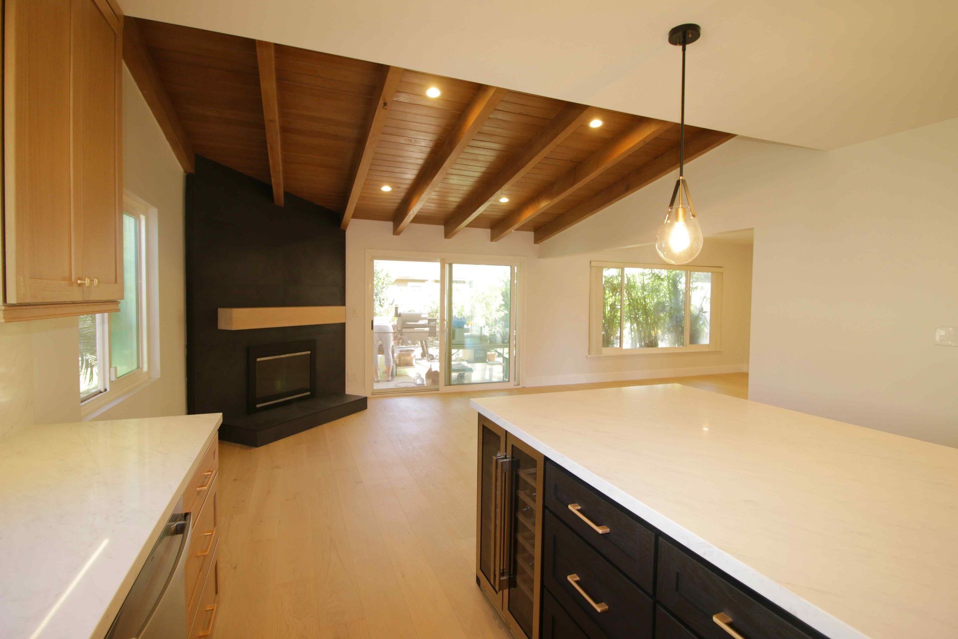 Modern kitchen with white countertops, dark cabinets, wood ceiling beams, and large windows.