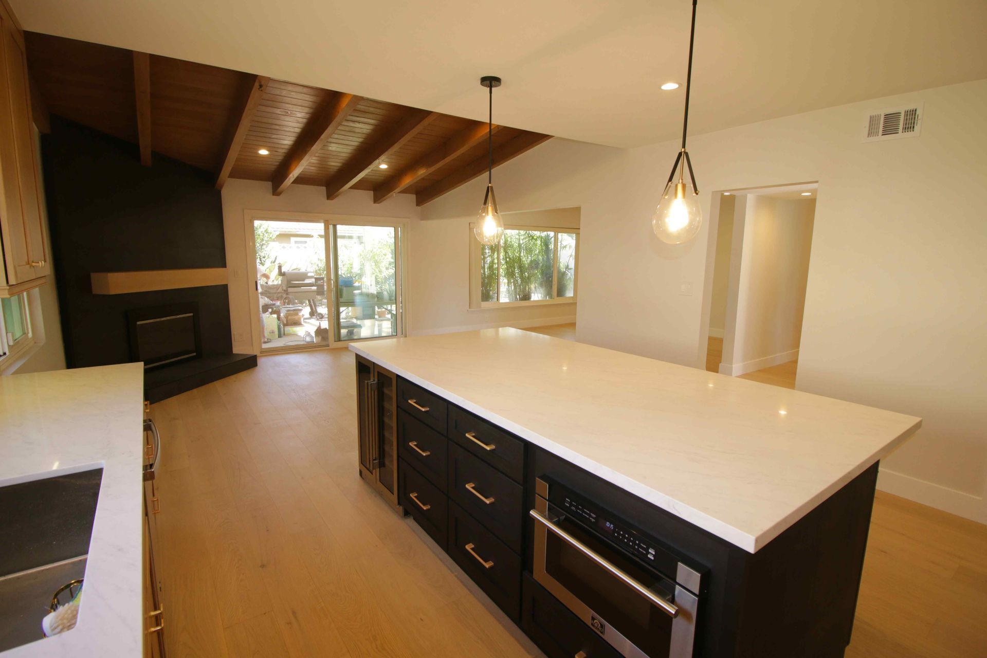 Modern kitchen with white island, dark cabinets, wood ceiling beams, and large windows