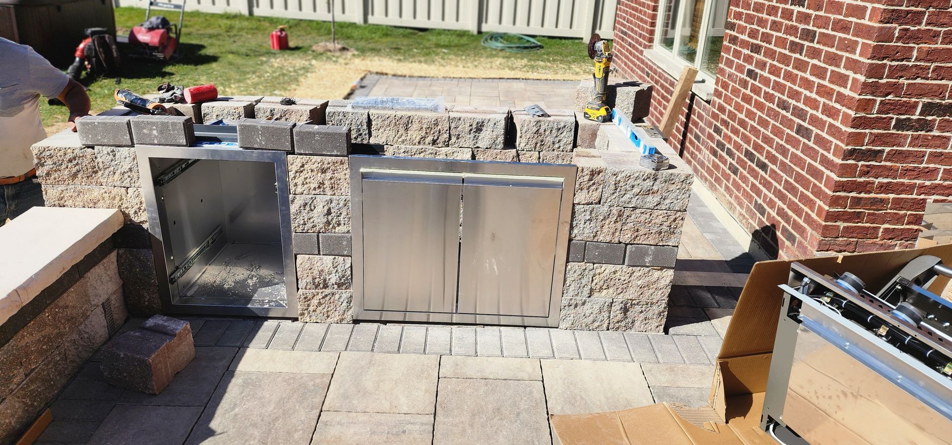 Outdoor kitchen island under construction with stone facade and stainless steel components.
