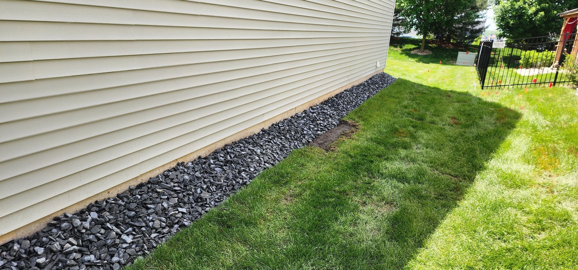 Side of a beige house with dark rocks along the base. Green grass is next to the rocks.