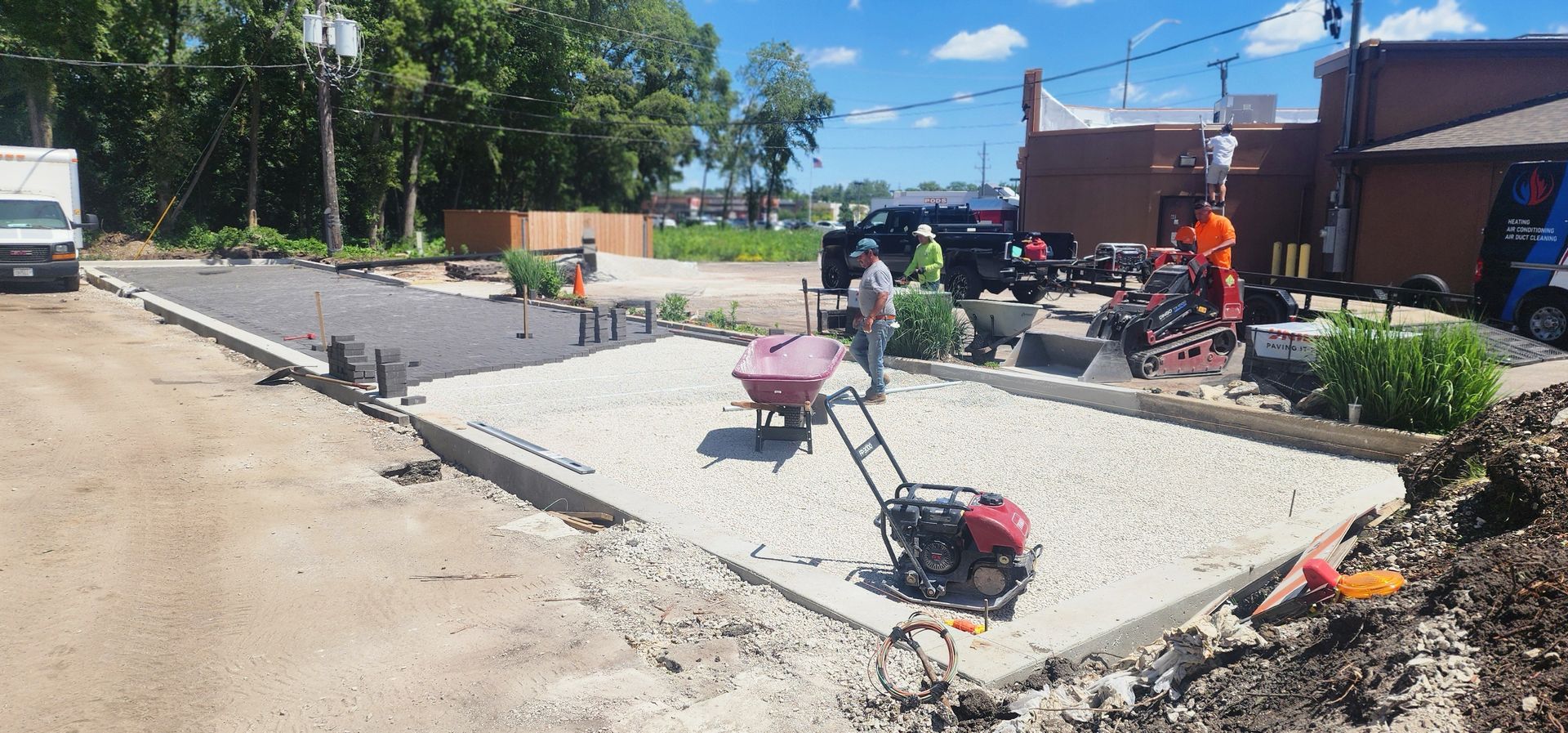 Construction workers paving a new patio area with machinery and wheelbarrows.