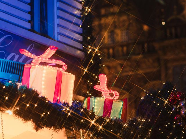 Lit-up holiday gifts with red ribbons and string lights in front of a building at night.
