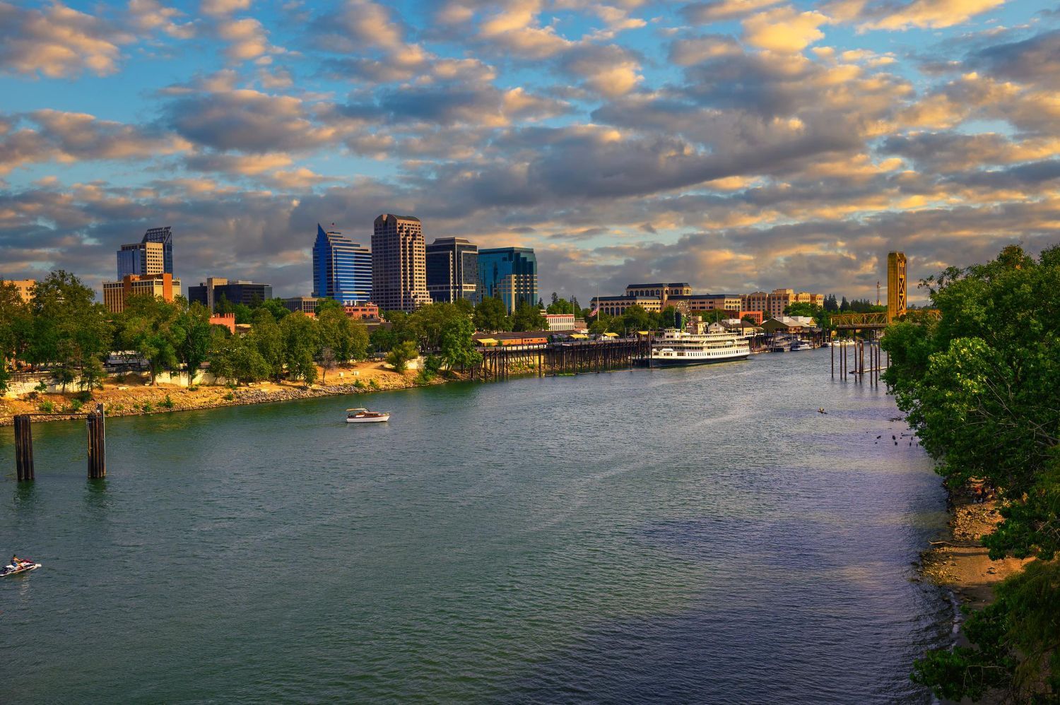 Sacramento skyline with river, trees, and cloudy sunset sky.