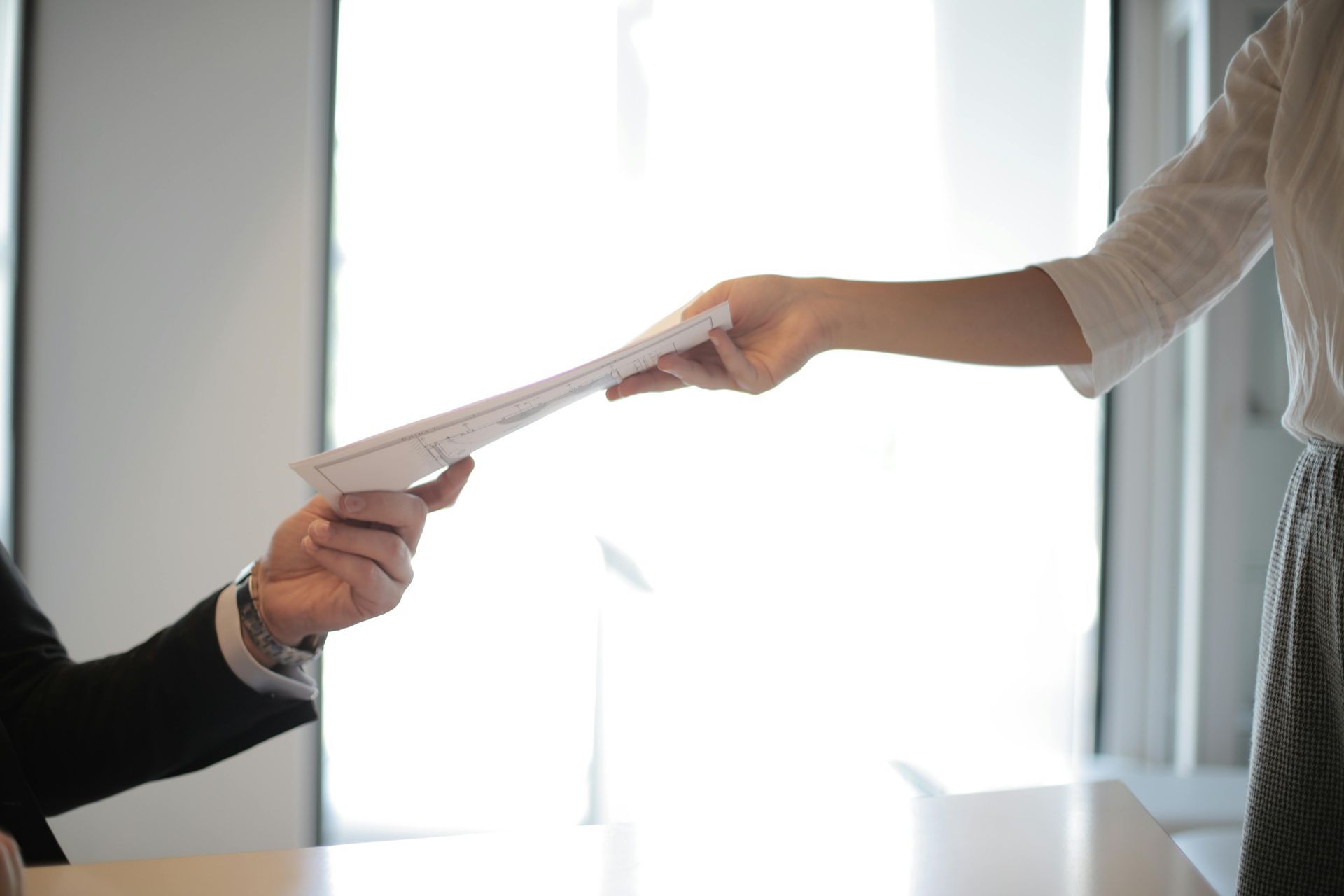Person in a suit receives papers from another person. They are in a well-lit office.