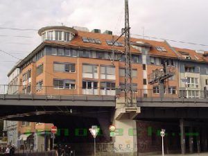 Unter einer Brücke steht ein großes Gebäude mit rotem Dach.
