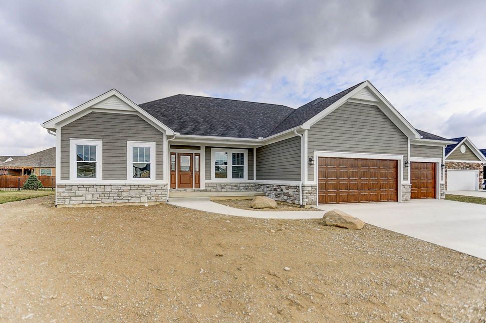 A large gray house with a brown garage door is sitting on top of a dirt field.