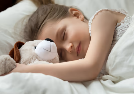 A little girl is sleeping in bed with a stuffed dog.
