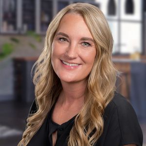 A woman with long blonde hair is smiling for the camera while wearing a black shirt.