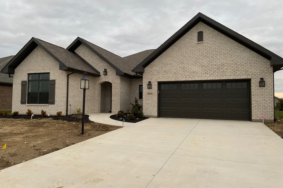 A large brick house with a black garage door is for sale.