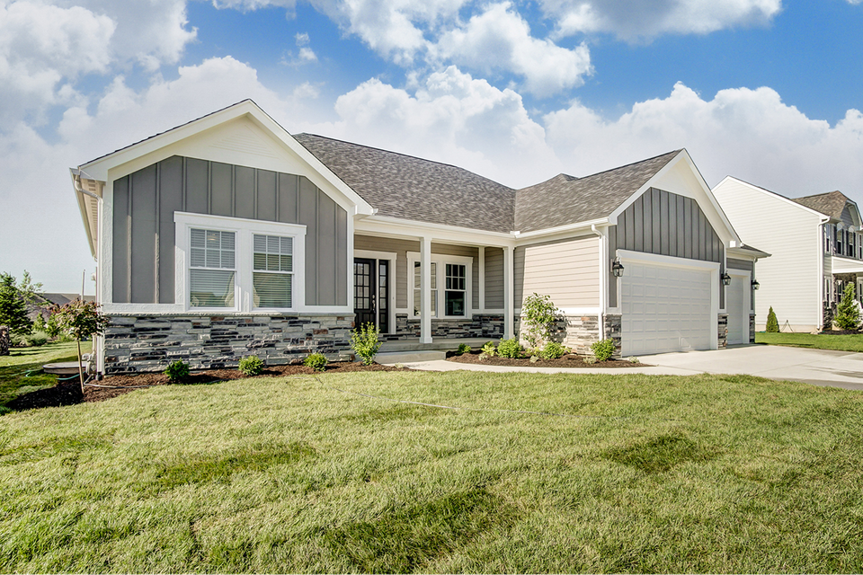 A house with a gray siding and a white trim is sitting on top of a lush green lawn.