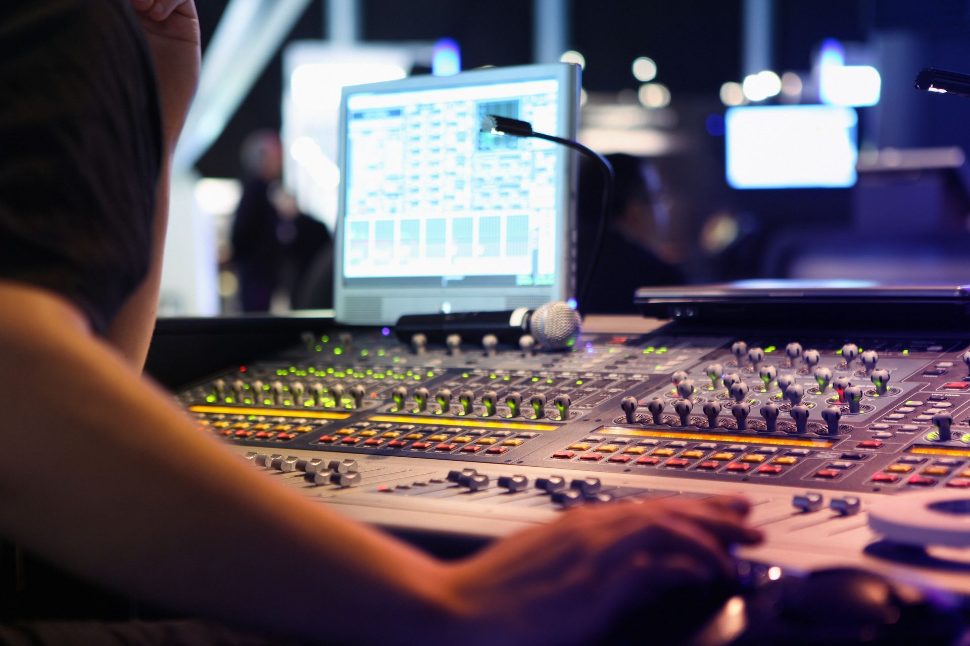 person operating a professional audio mixing console and computer screen displaying audio software is visible in the background person operating a professional audio mixing console and computer screen displaying audio software is visible in the background