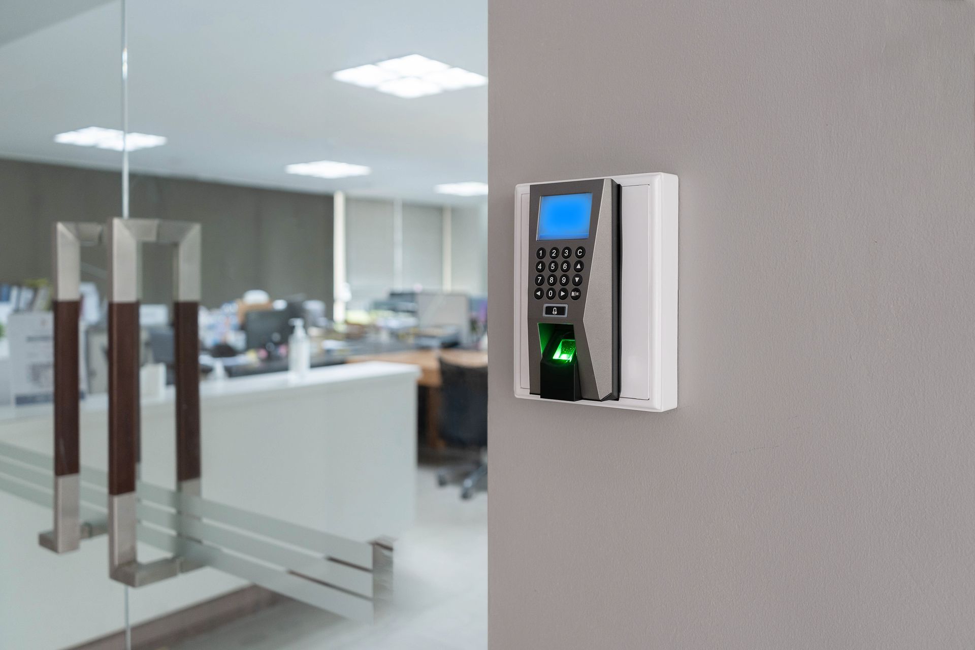 biometric fingerprint scanner mounted on a gray wall next to a glass door with metal handles, used for secure access control biometric fingerprint scanner mounted on a gray wall next to a glass door with metal handles, used for secure access control