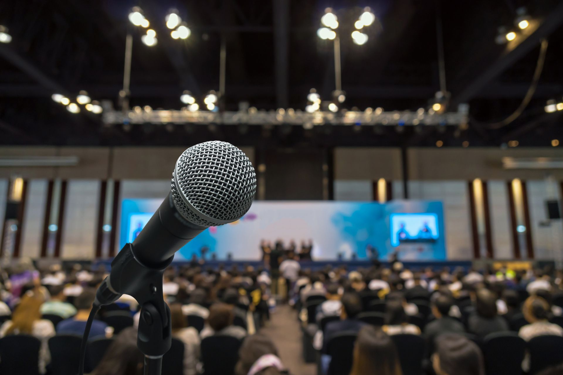 microphone in sharp focus with a large audience in a conference or public speaking event microphone in sharp focus with a large audience in a conference or public speaking event