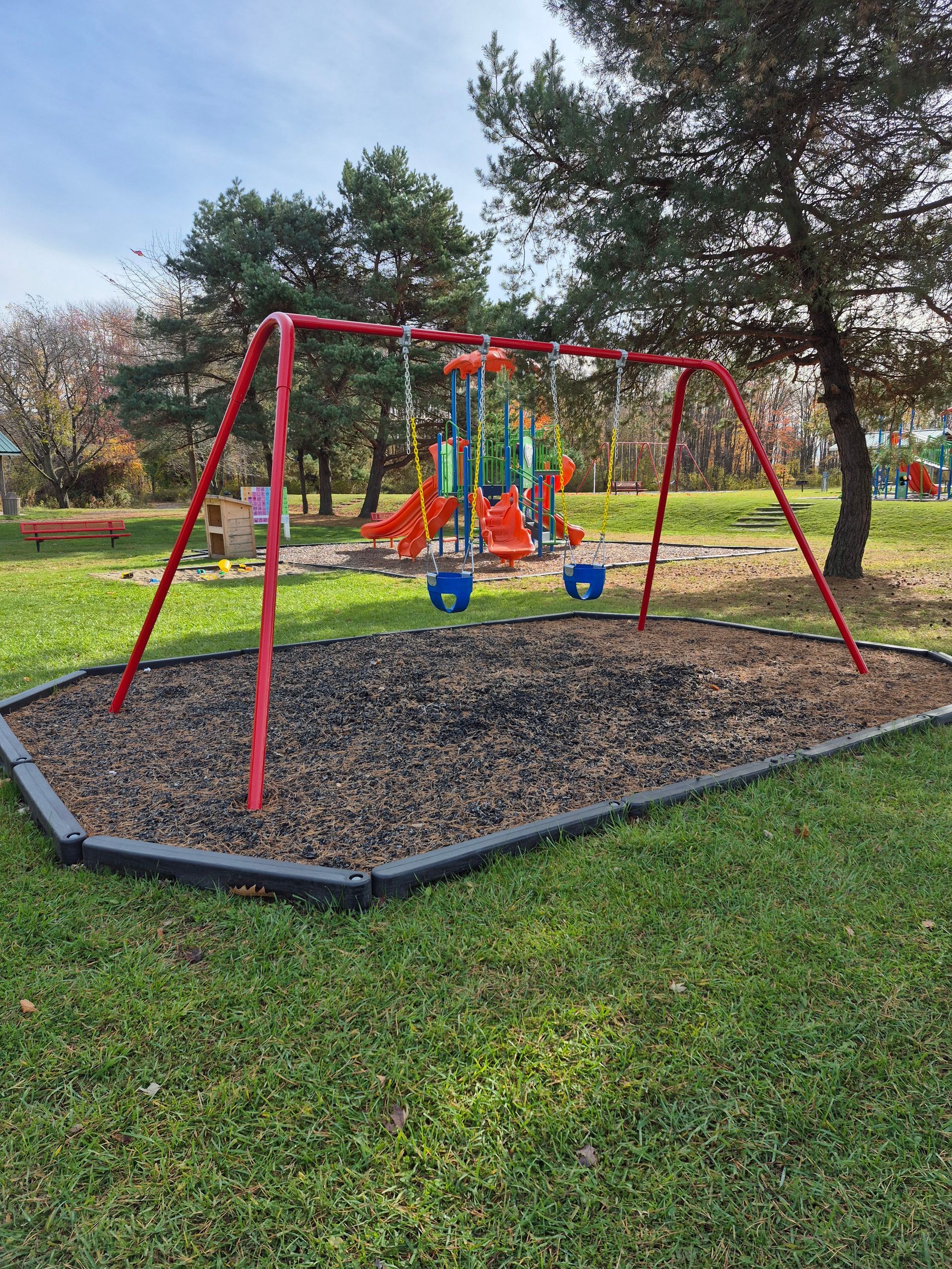 Children’s playground with red swings over a black mulch pad in a grassy park