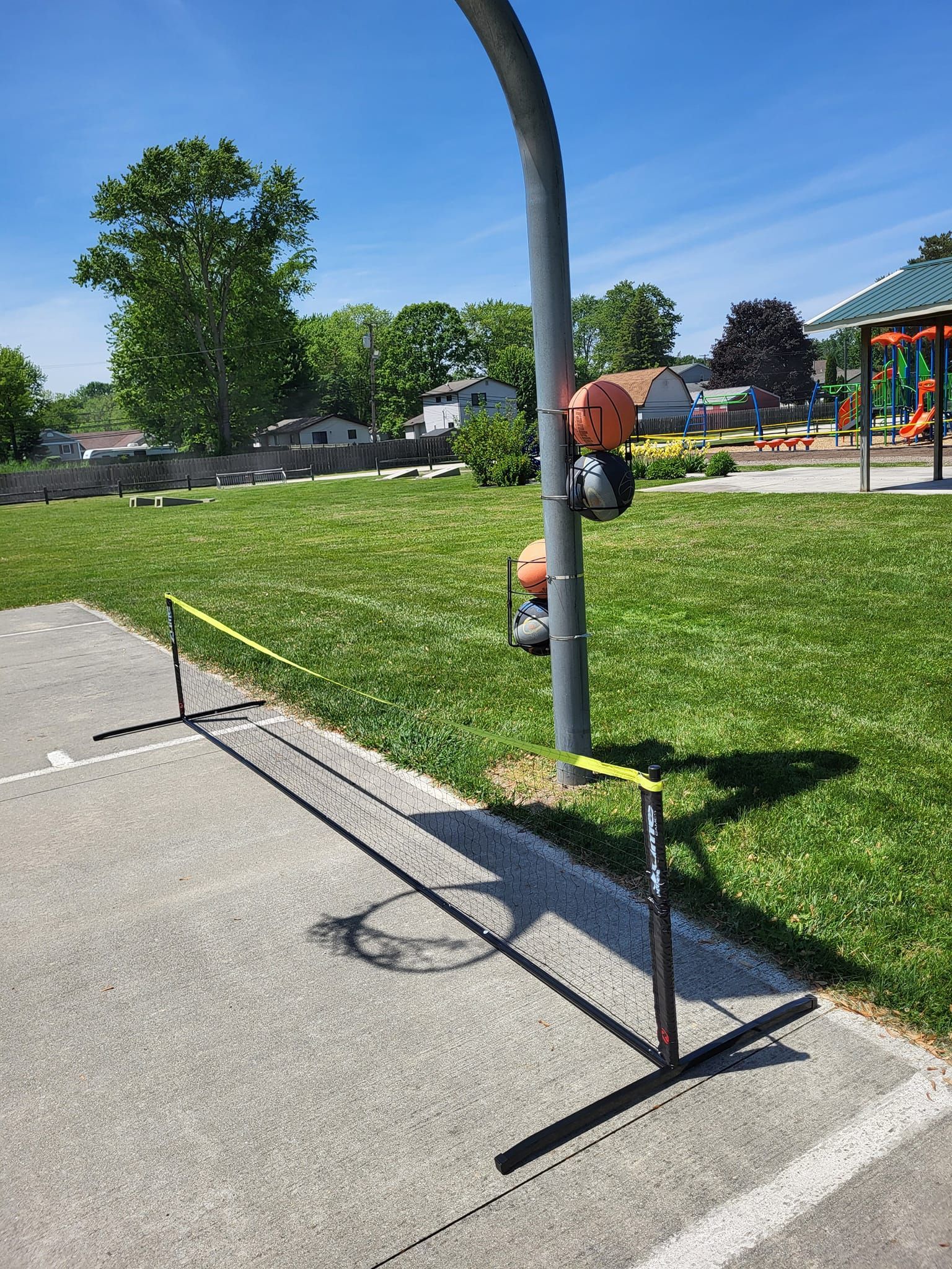 Pole-mounted parking payment station beside a grassy park path and playground on a sunny day