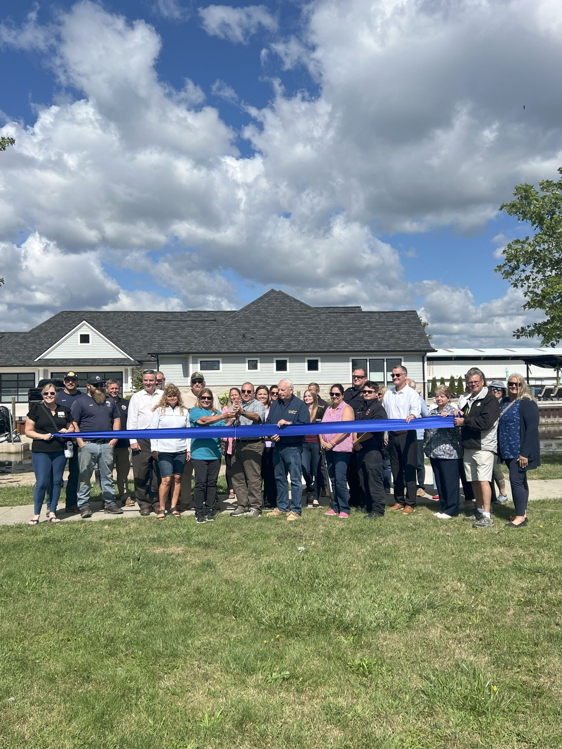 Group of people at a ribbon-cutting ceremony in front of a house under a cloudy sky