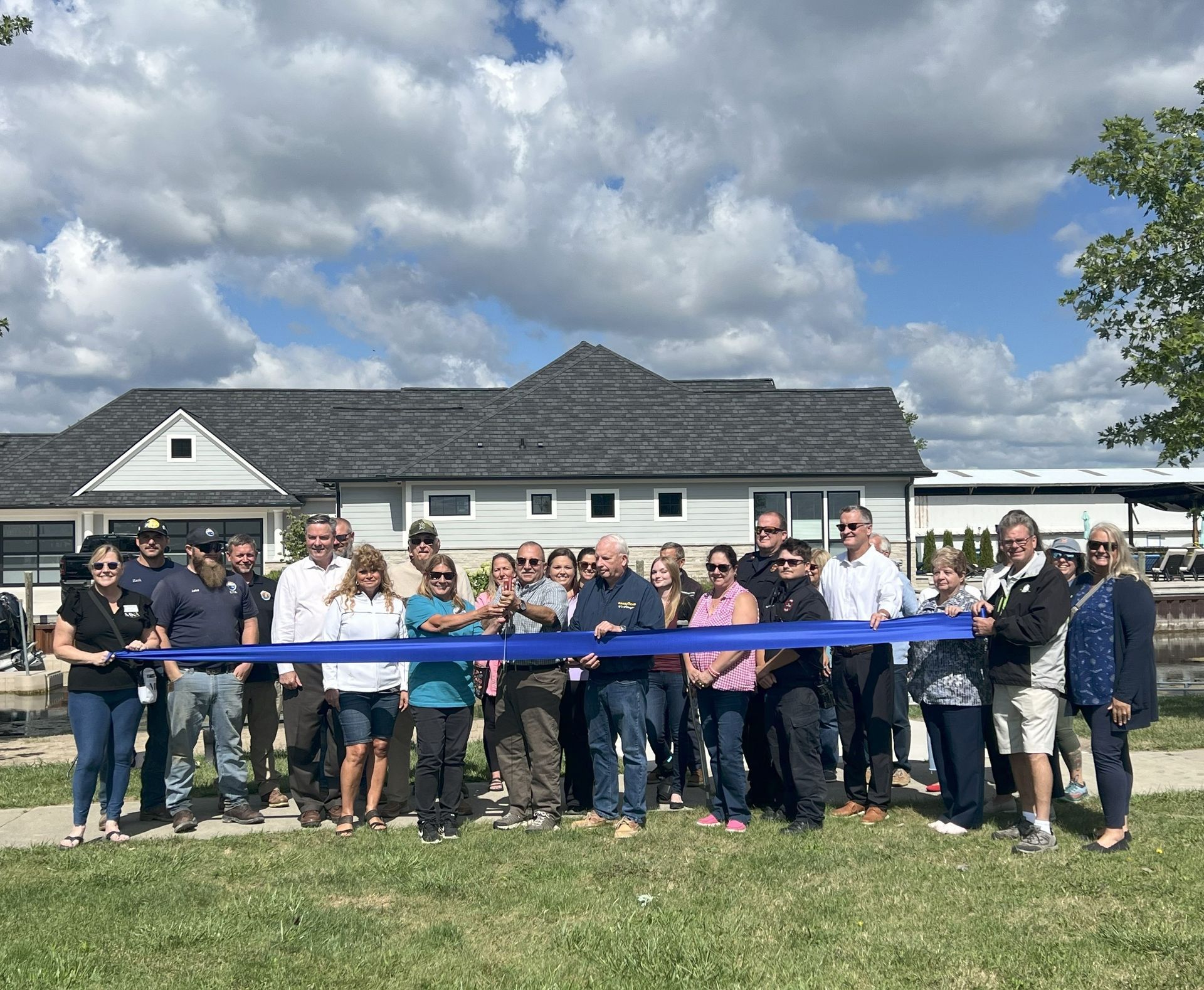 Group of people at a ribbon-cutting ceremony in front of a large building under a cloudy sky.