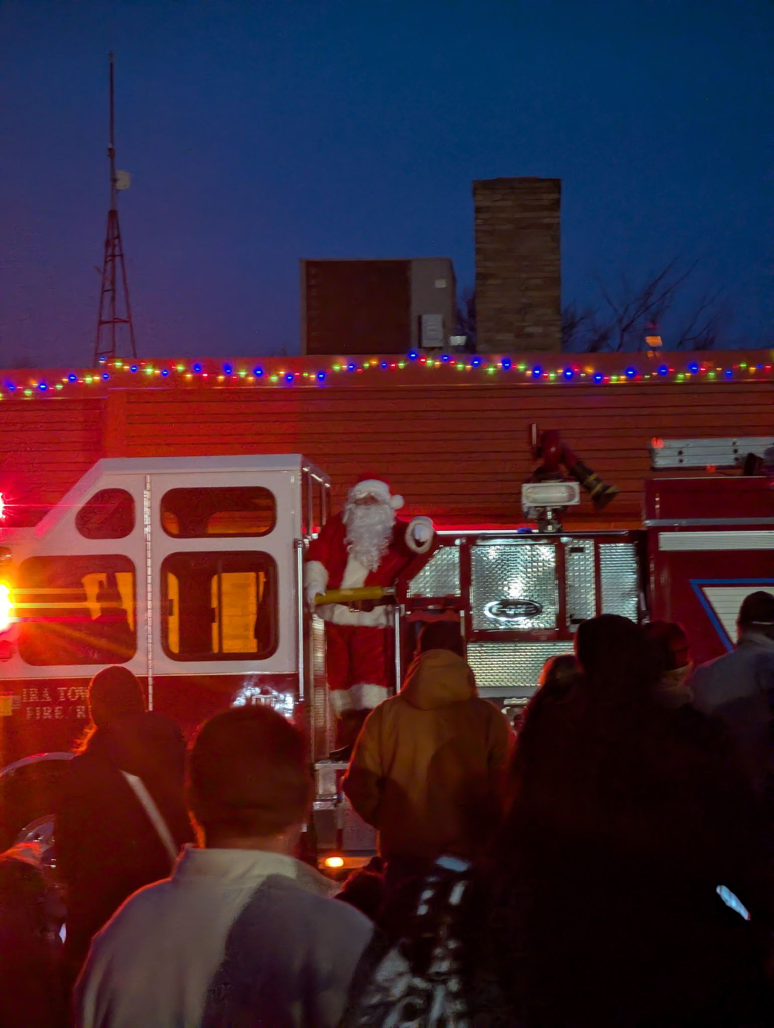 Firetruck at night with flashing red lights and firefighters near a building rooftop.