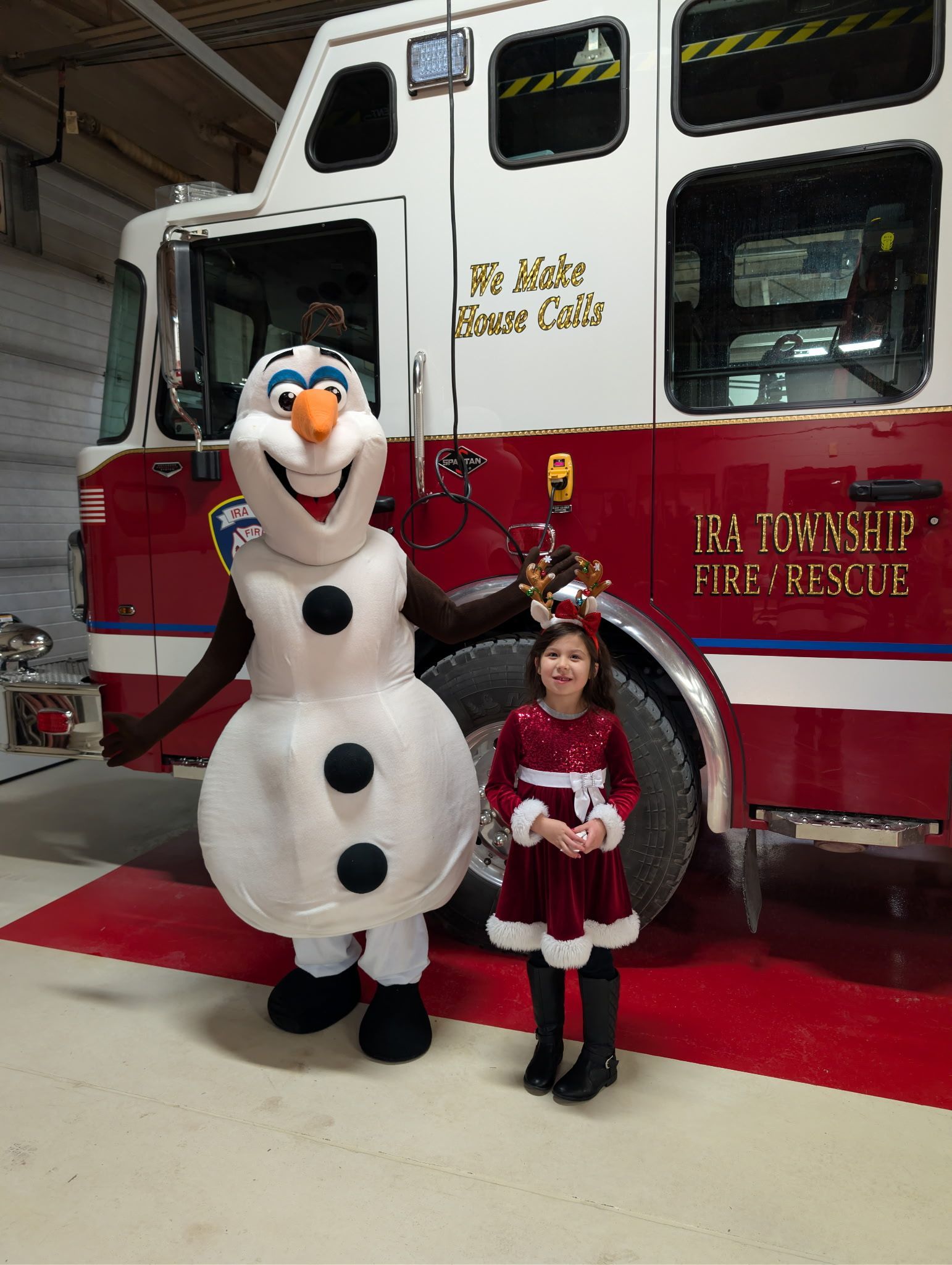 Olaf mascot and a child posing in front of a red-and-white fire rescue truck indoors