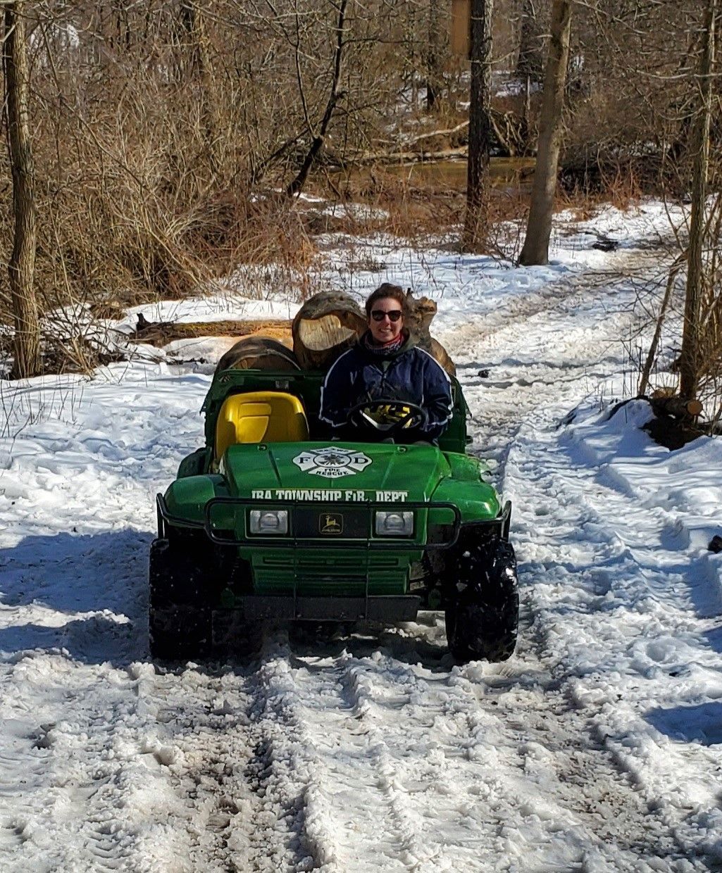 Green ATV with two riders driving through a snowy wooded trail