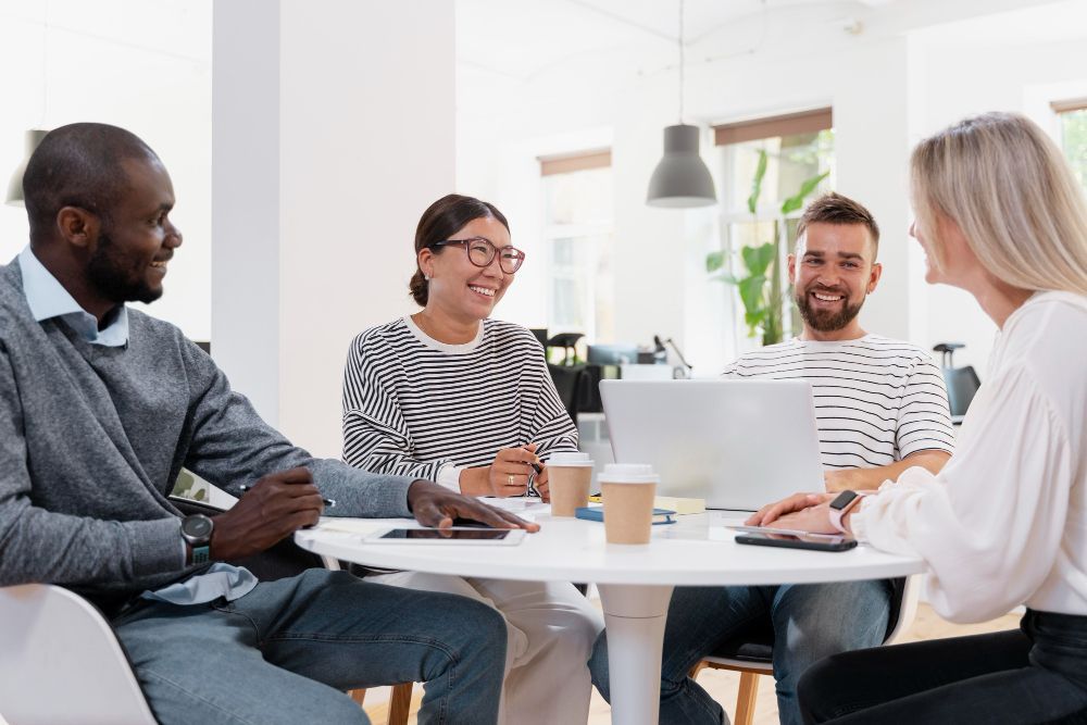 group of people are sitting around a table with laptops
