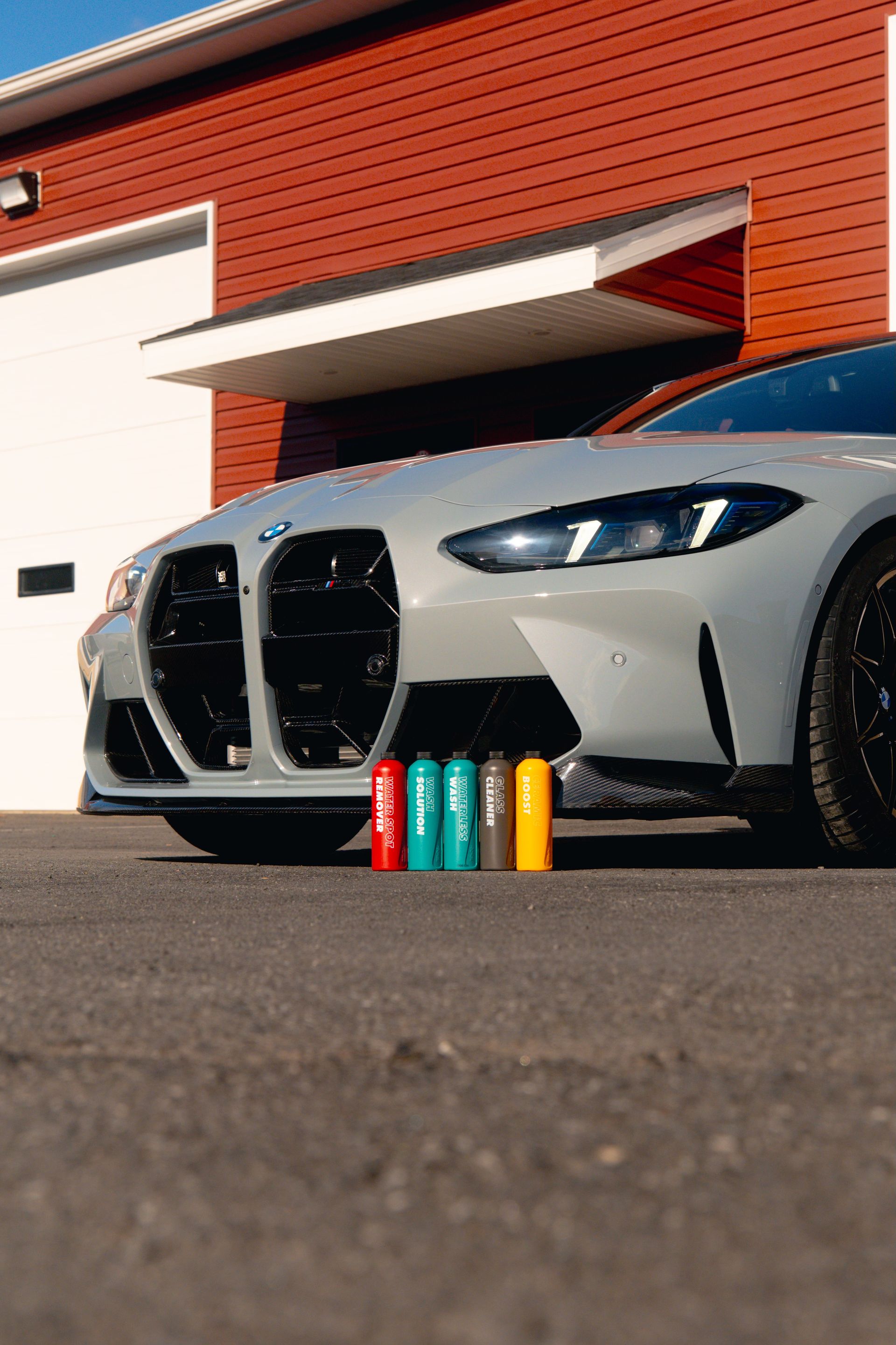 Silver sports car parked outside a building, with colorful batteries lined up in front of the bumper