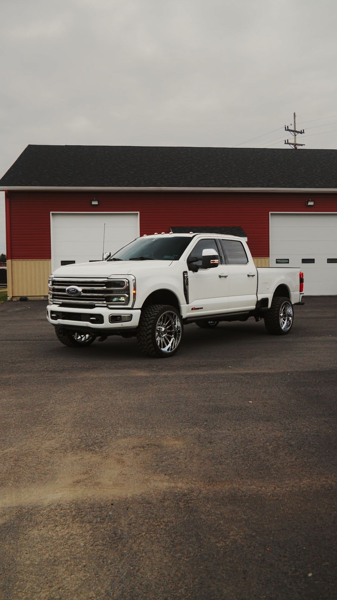 White pickup truck parked in front of a red building with garage doors under a gray sky