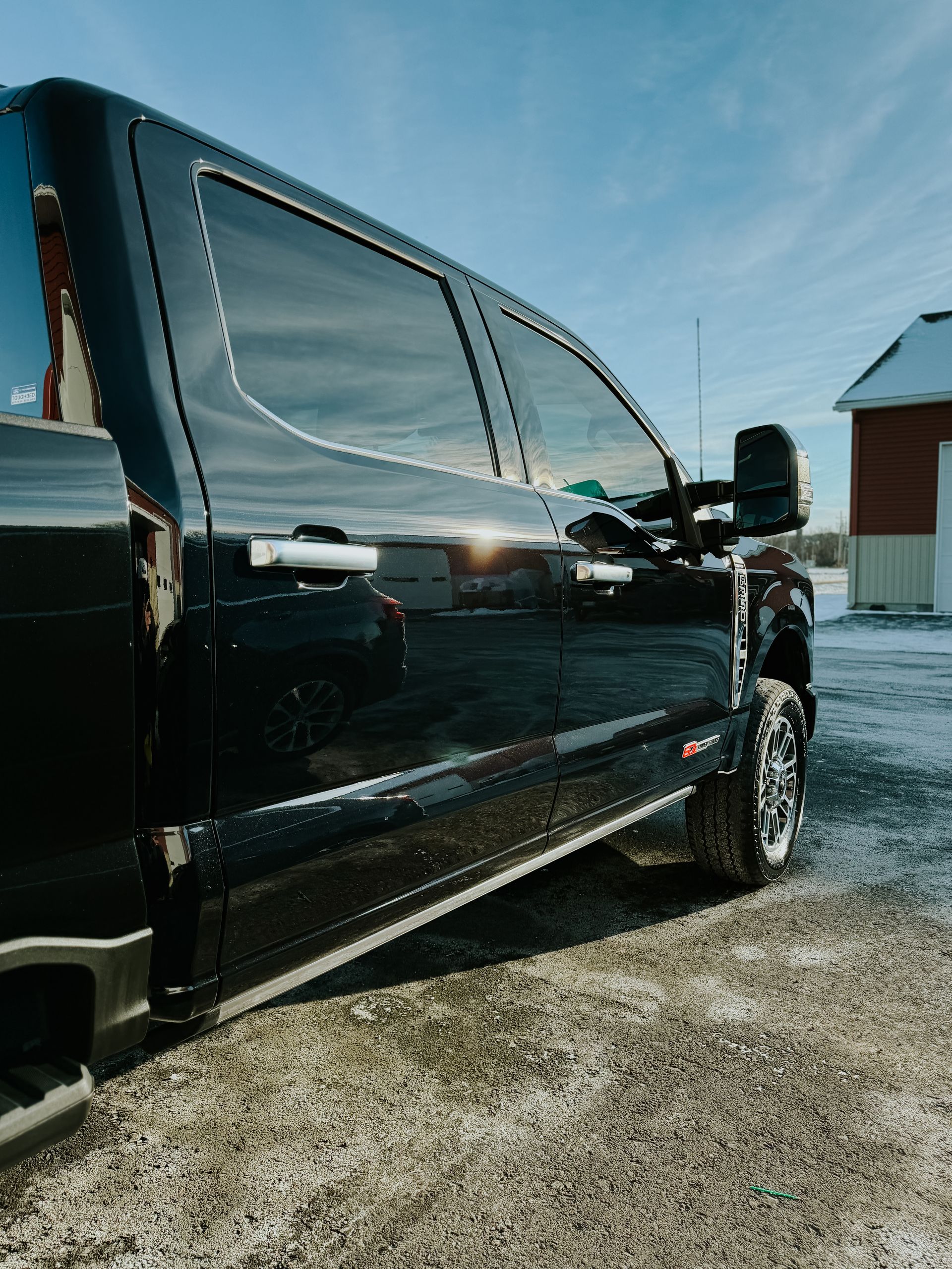 Black pickup truck parked on gravel beside a red building under a blue sky