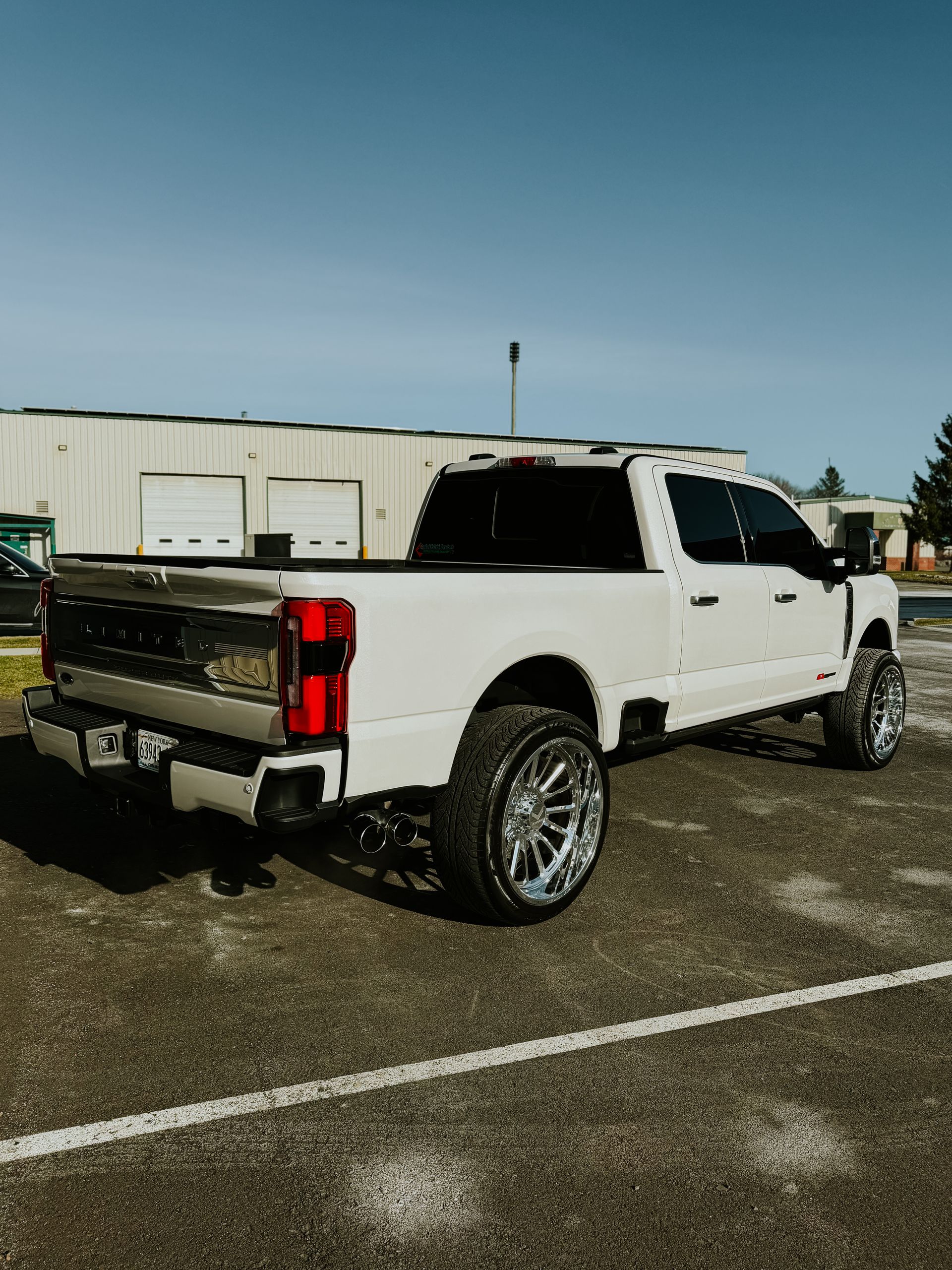 White lifted pickup truck parked in a lot beside a white industrial building.