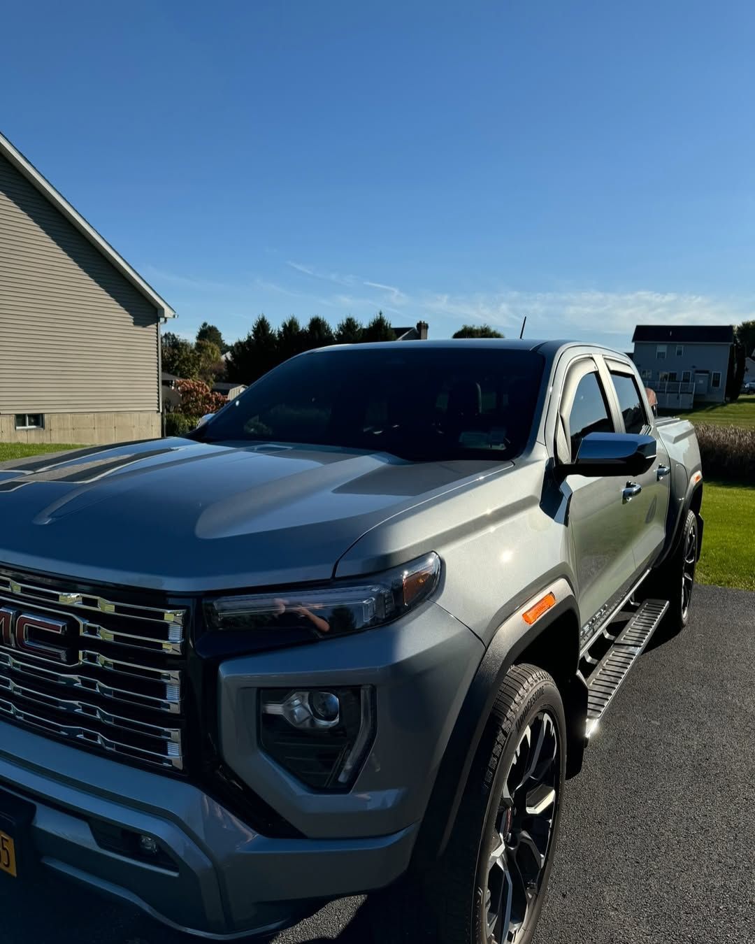 Silver GMC pickup truck parked on a gravel driveway beside a house under a clear blue sky