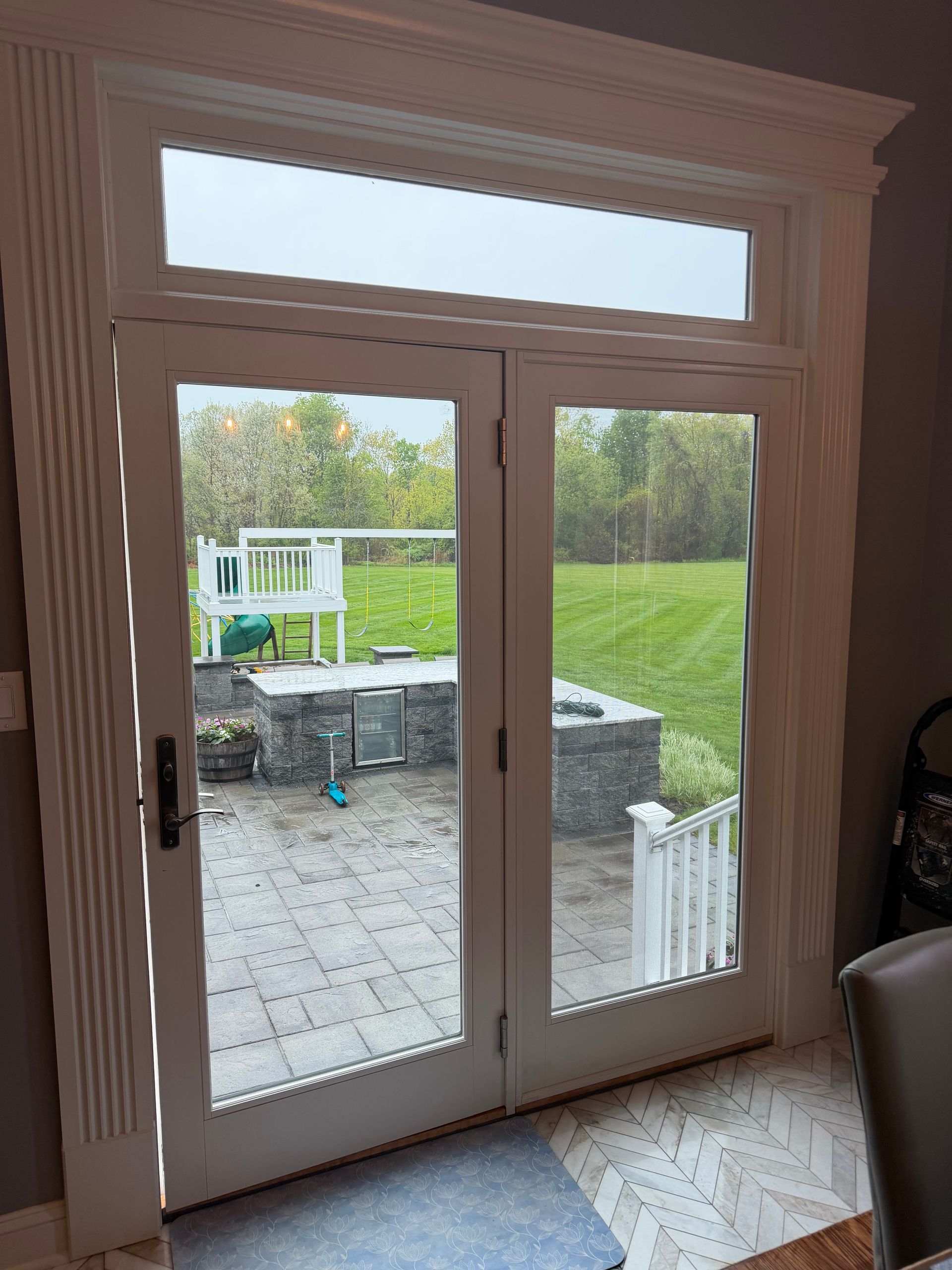 Interior view through white French doors to a patio and green yard with a stone wall and gazebo