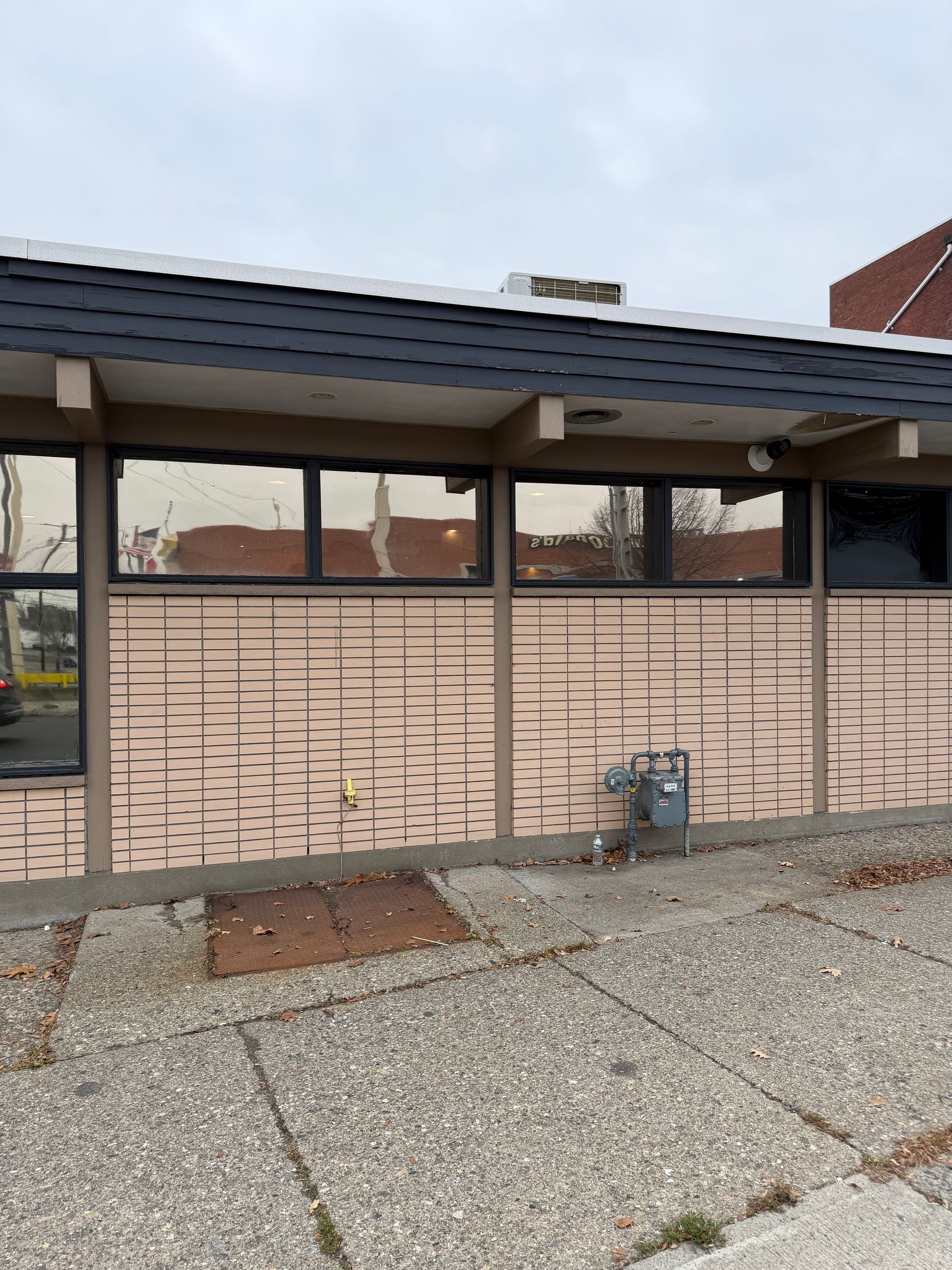 Exterior of a beige building with dark windows, a metal roof, and gravel ground