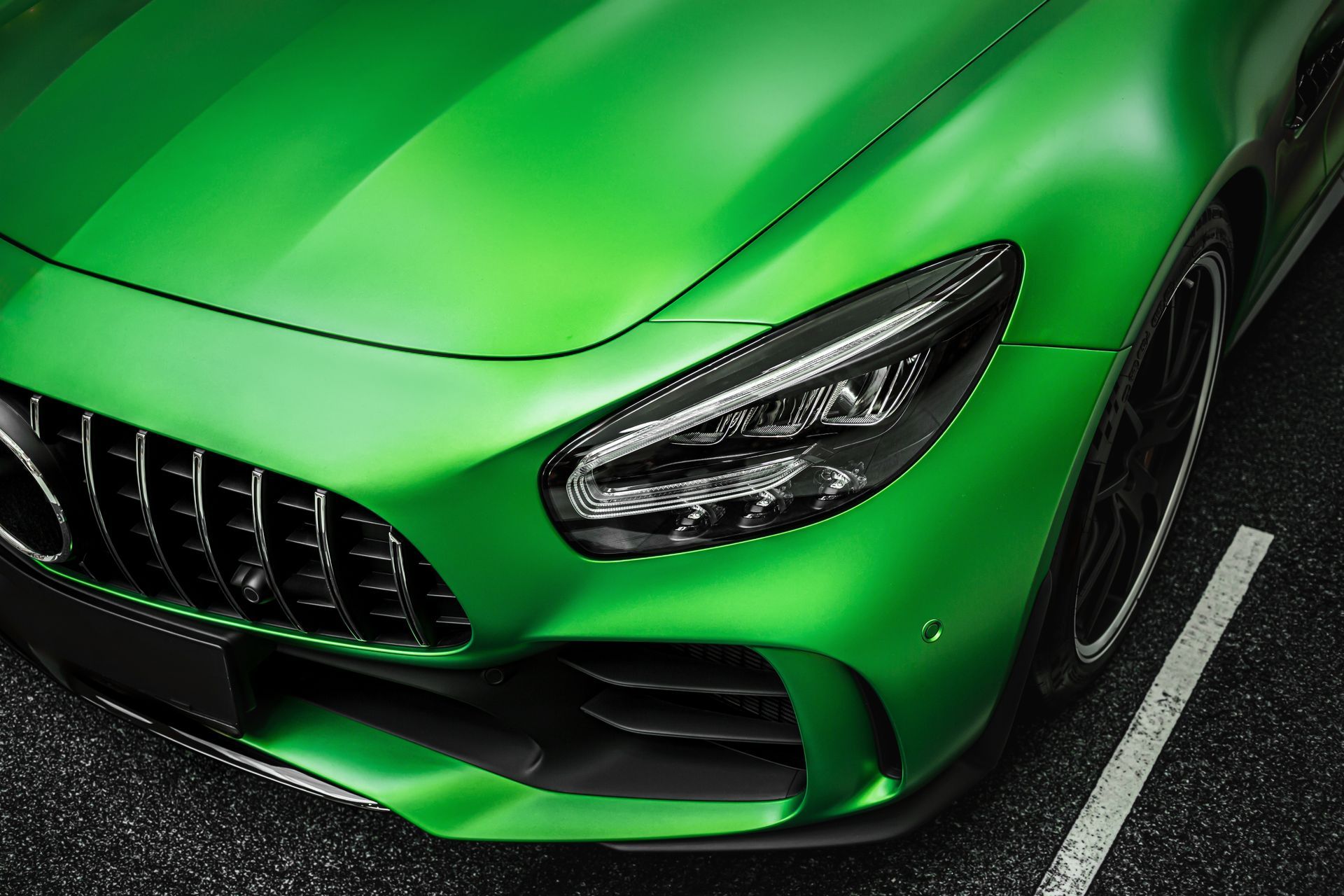 Green sports car front end parked on asphalt, close-up of grille and headlight.