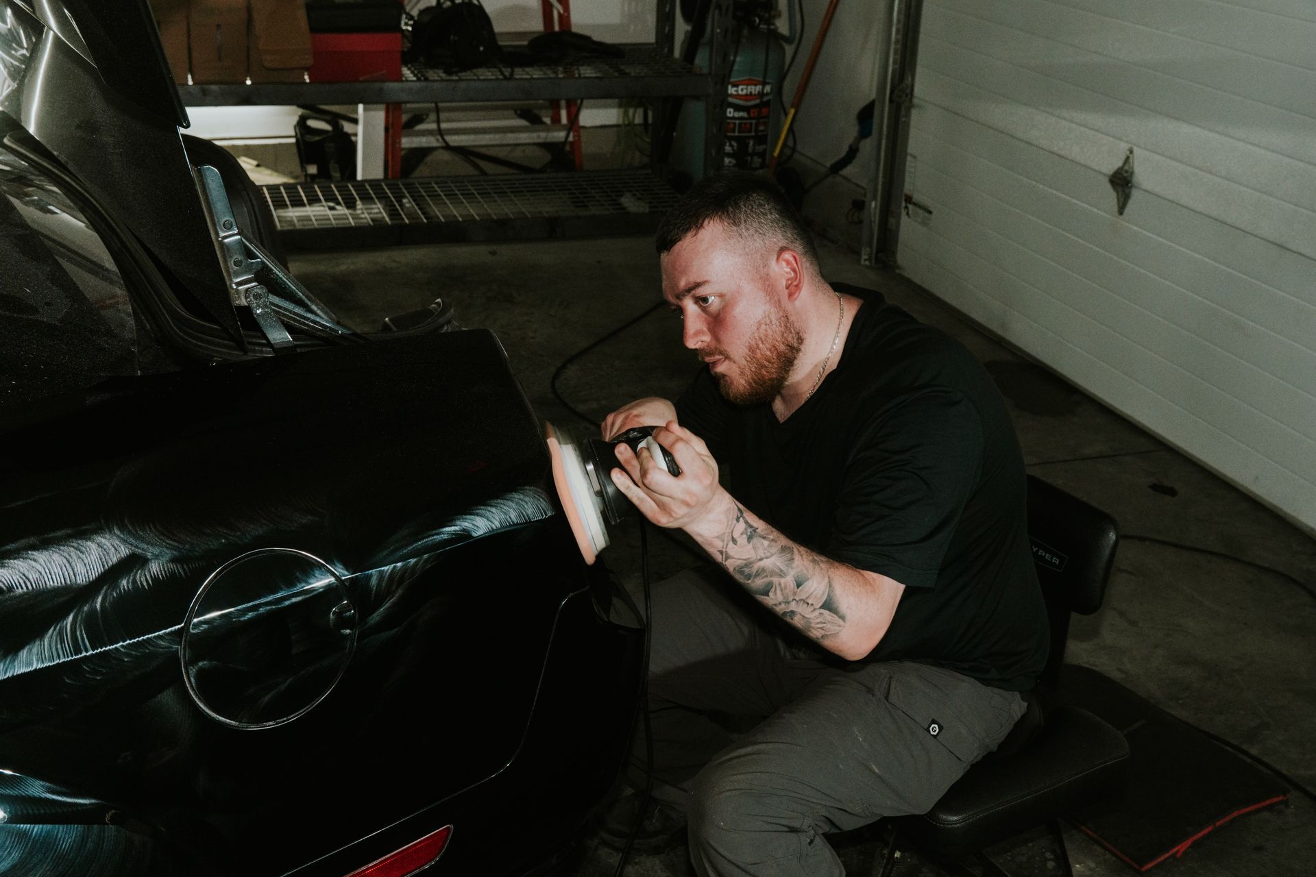 Man polishing the black front bumper of a car in a garage