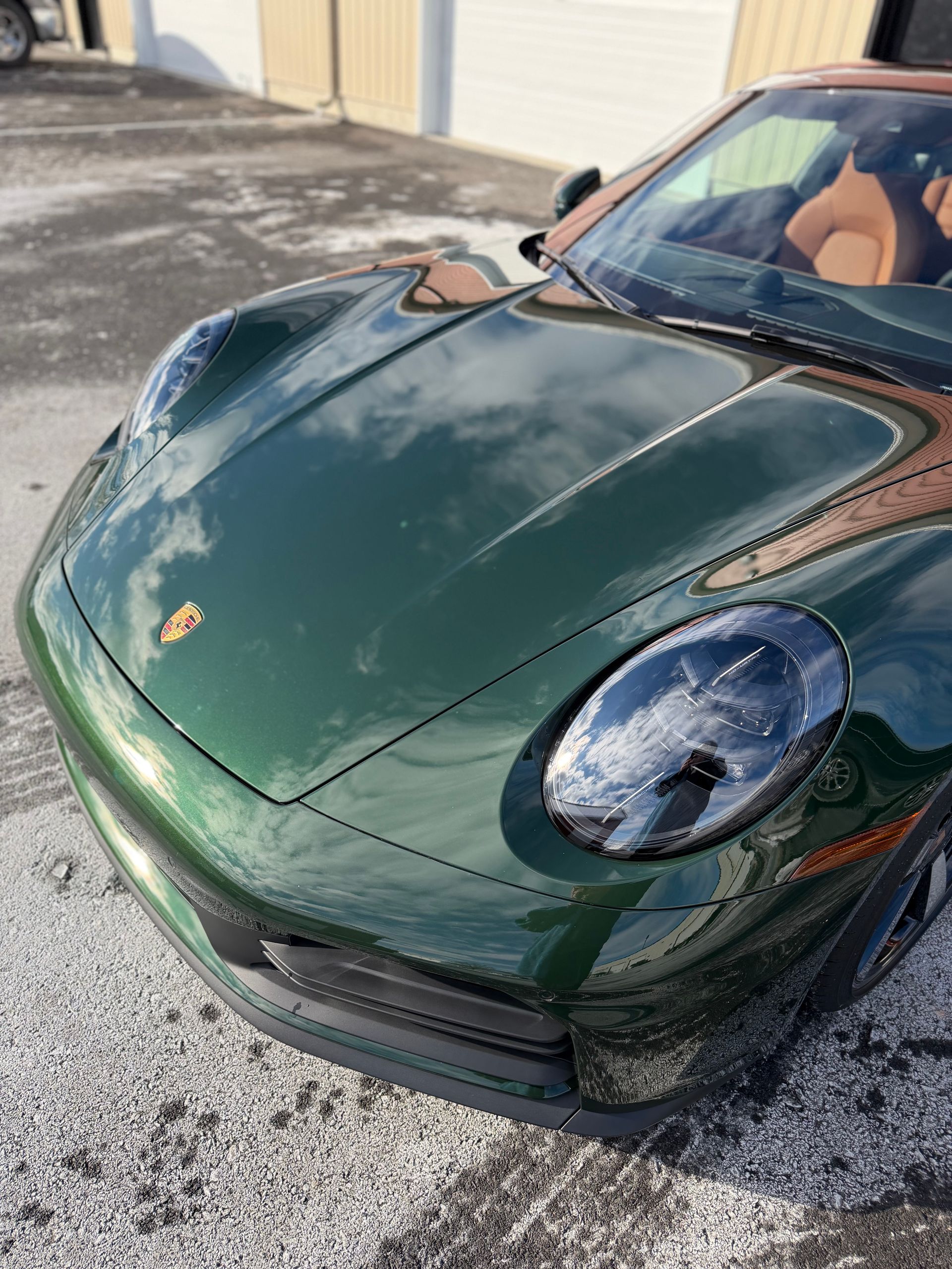 Green Porsche sports car hood and front end parked outdoors, with a dent and chipped paint on the hood.