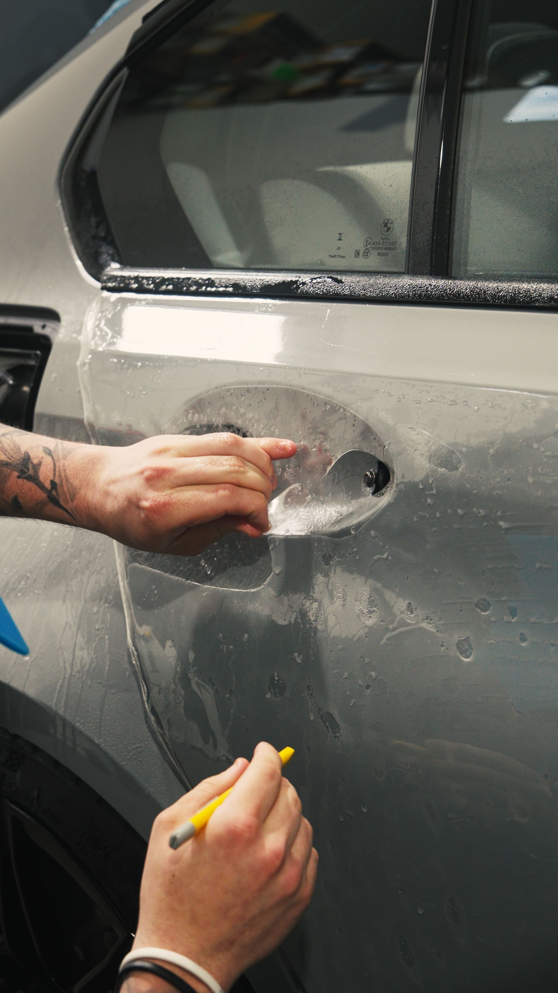 Hands washing a gray car door with soap and water at a car wash