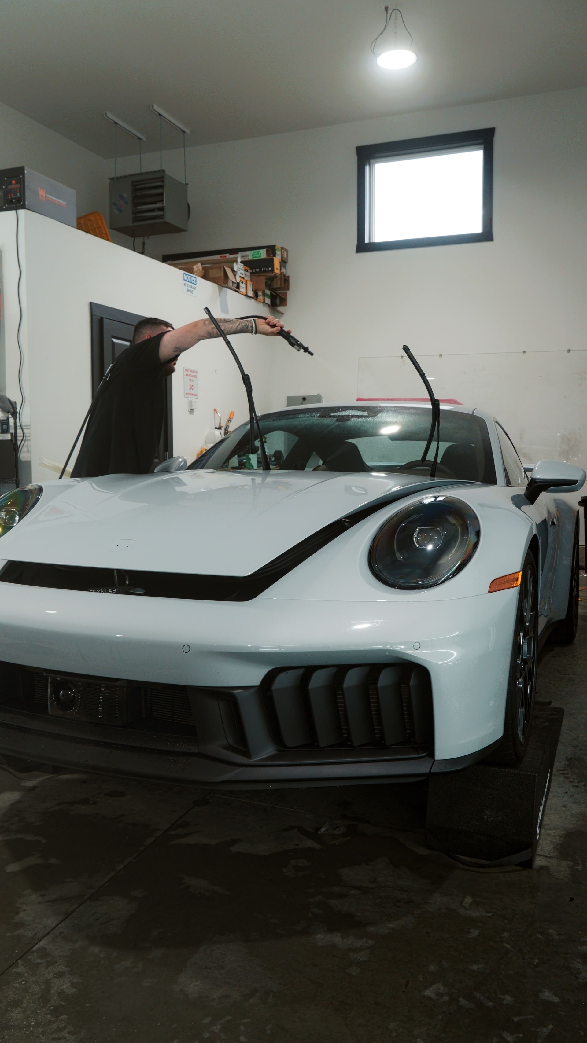 White sports car in a garage with its hood open and a person working near the windshield.