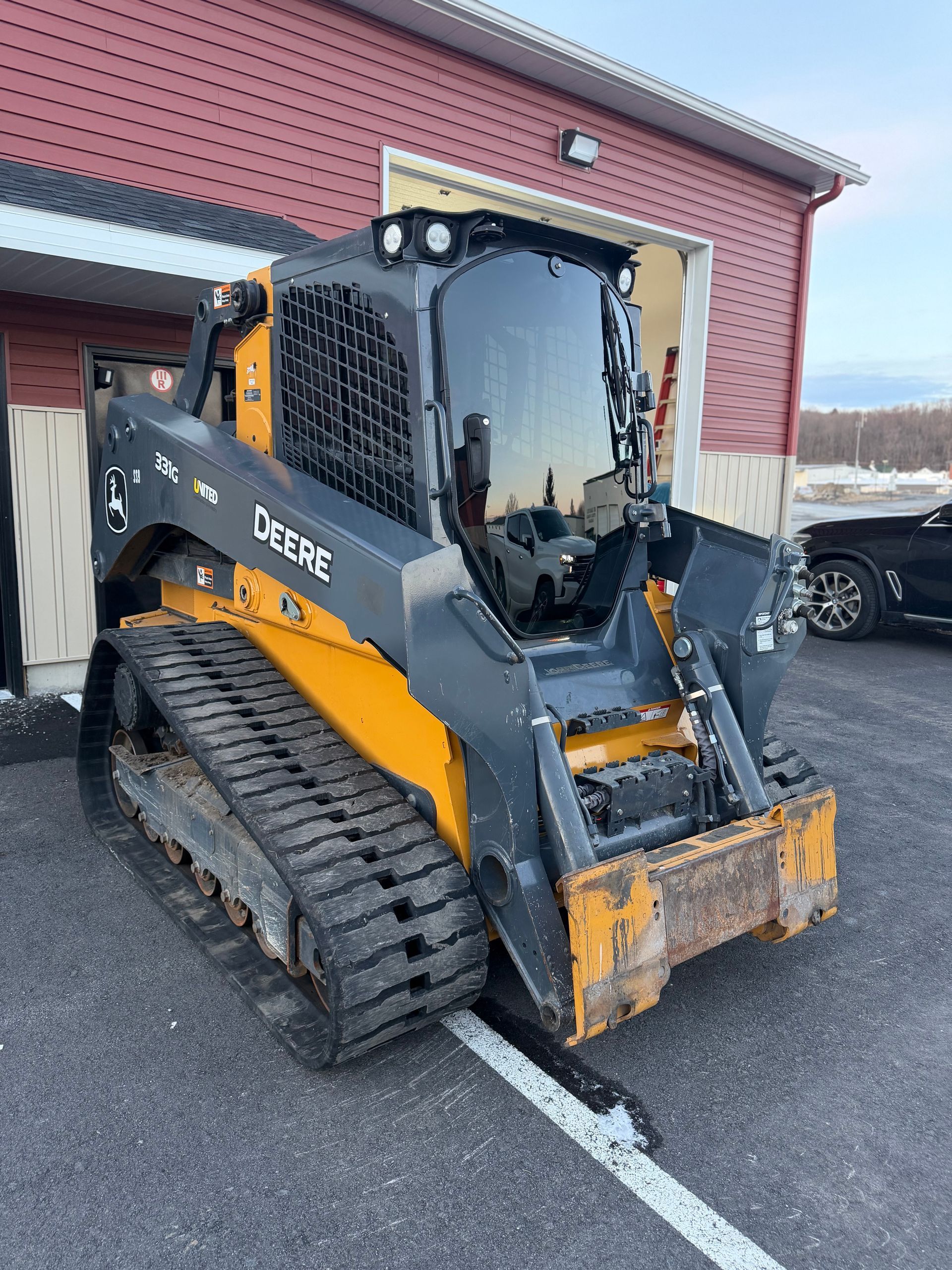 Orange and black compact track loader parked outside a red building on a snowy lot