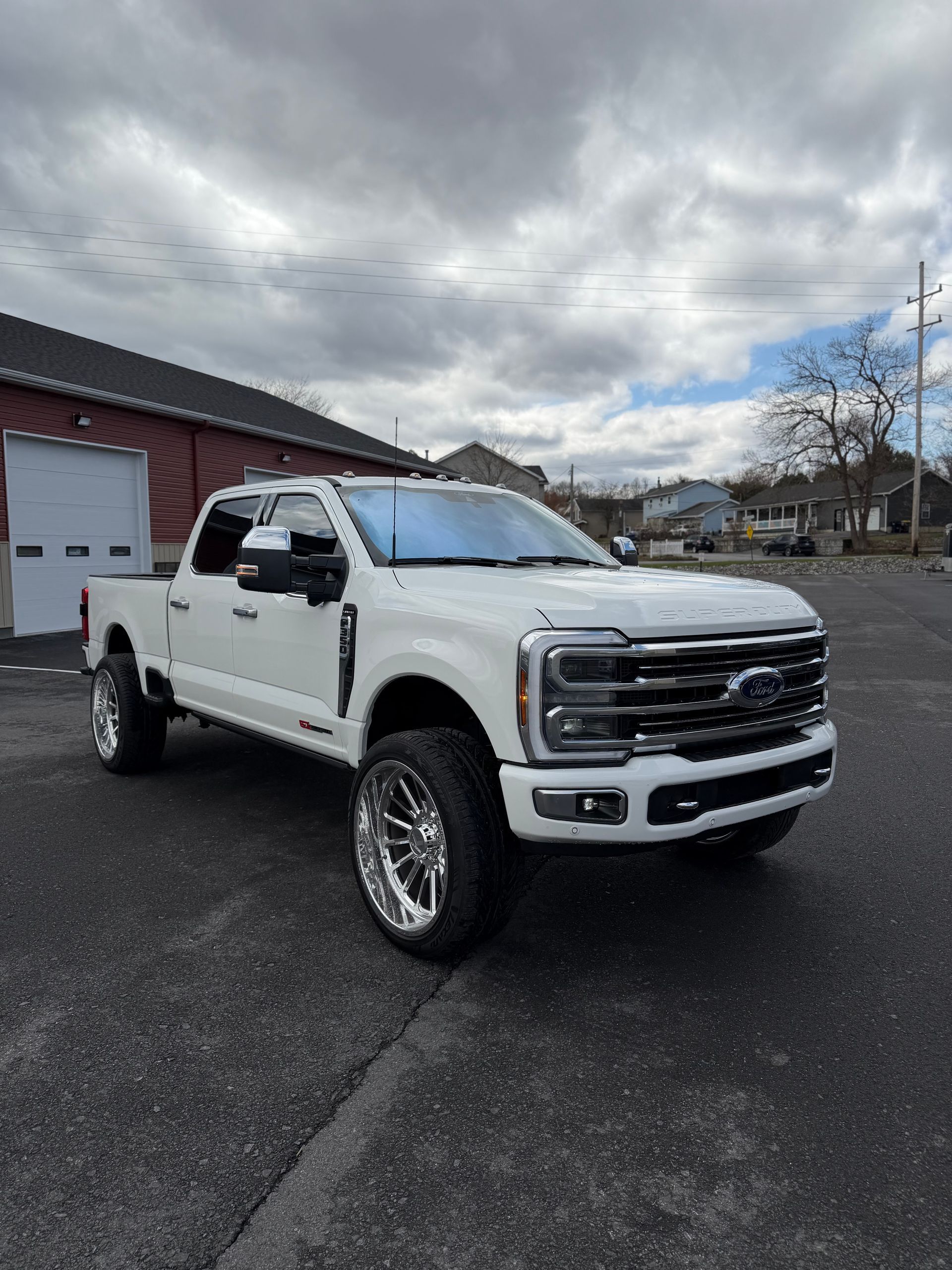 White lifted pickup truck parked outside a garage under cloudy skies.