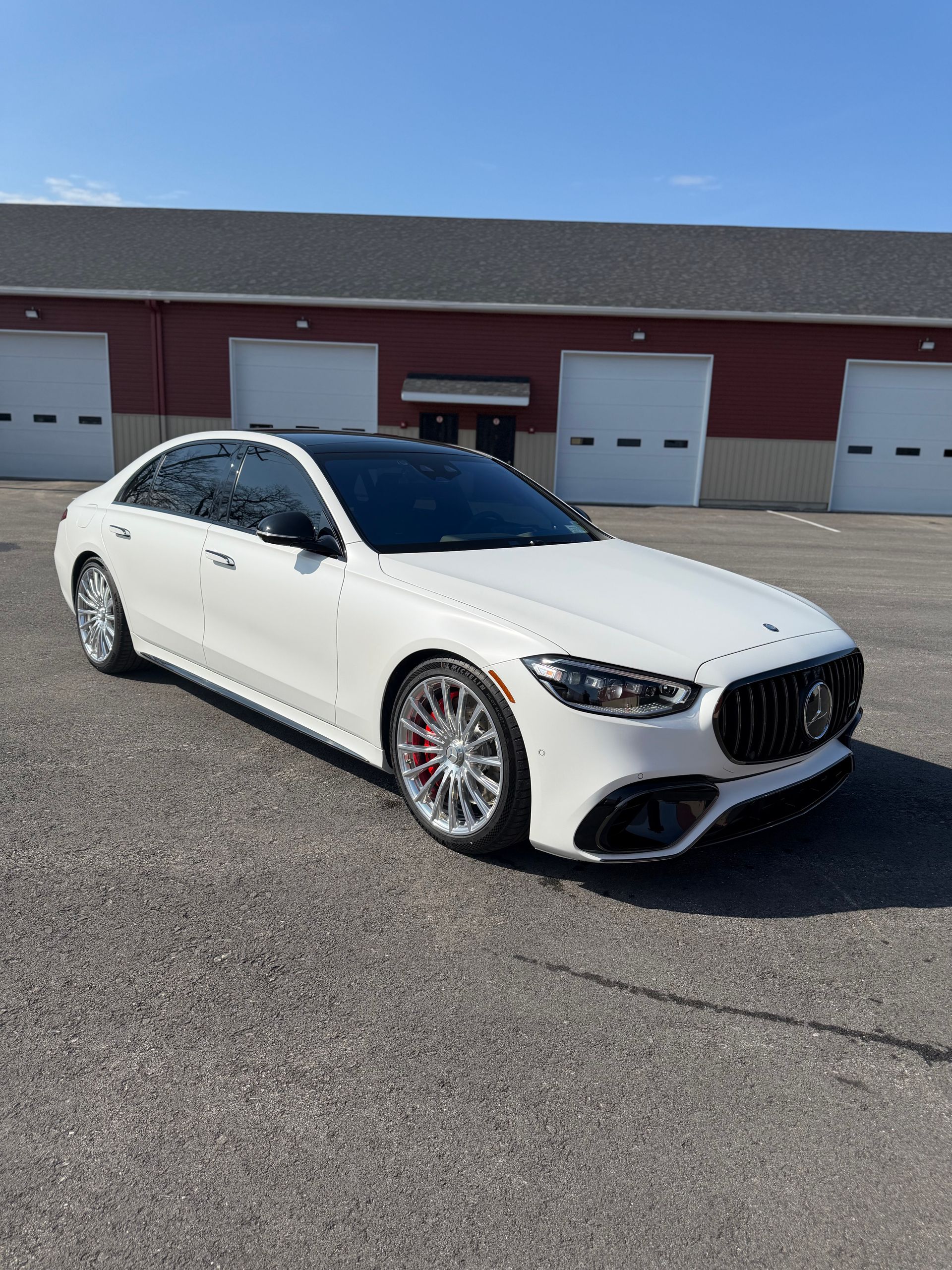 White sports sedan parked in front of red garage doors on a sunny day