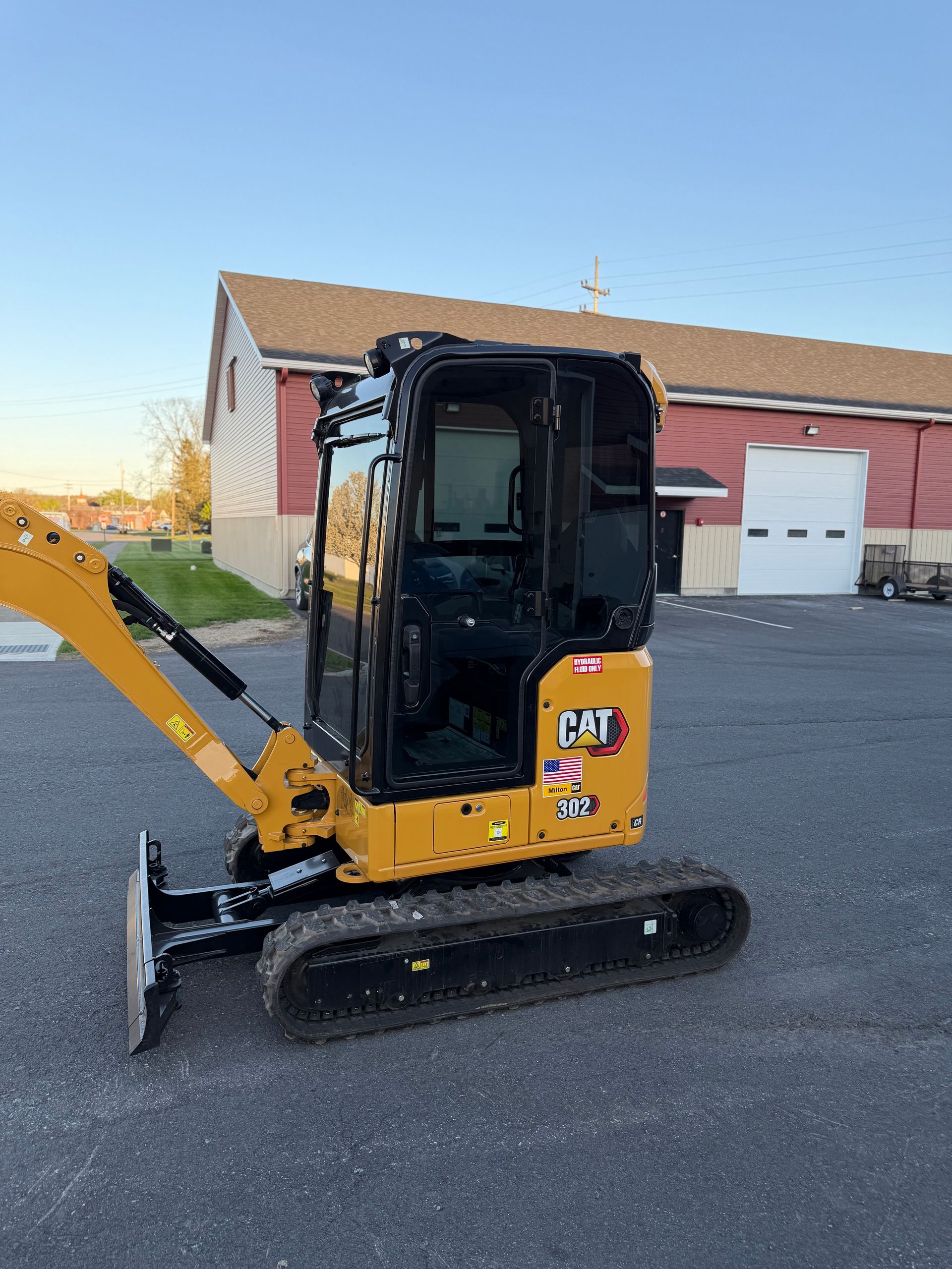 Yellow and black mini excavator on pavement outside a brick building