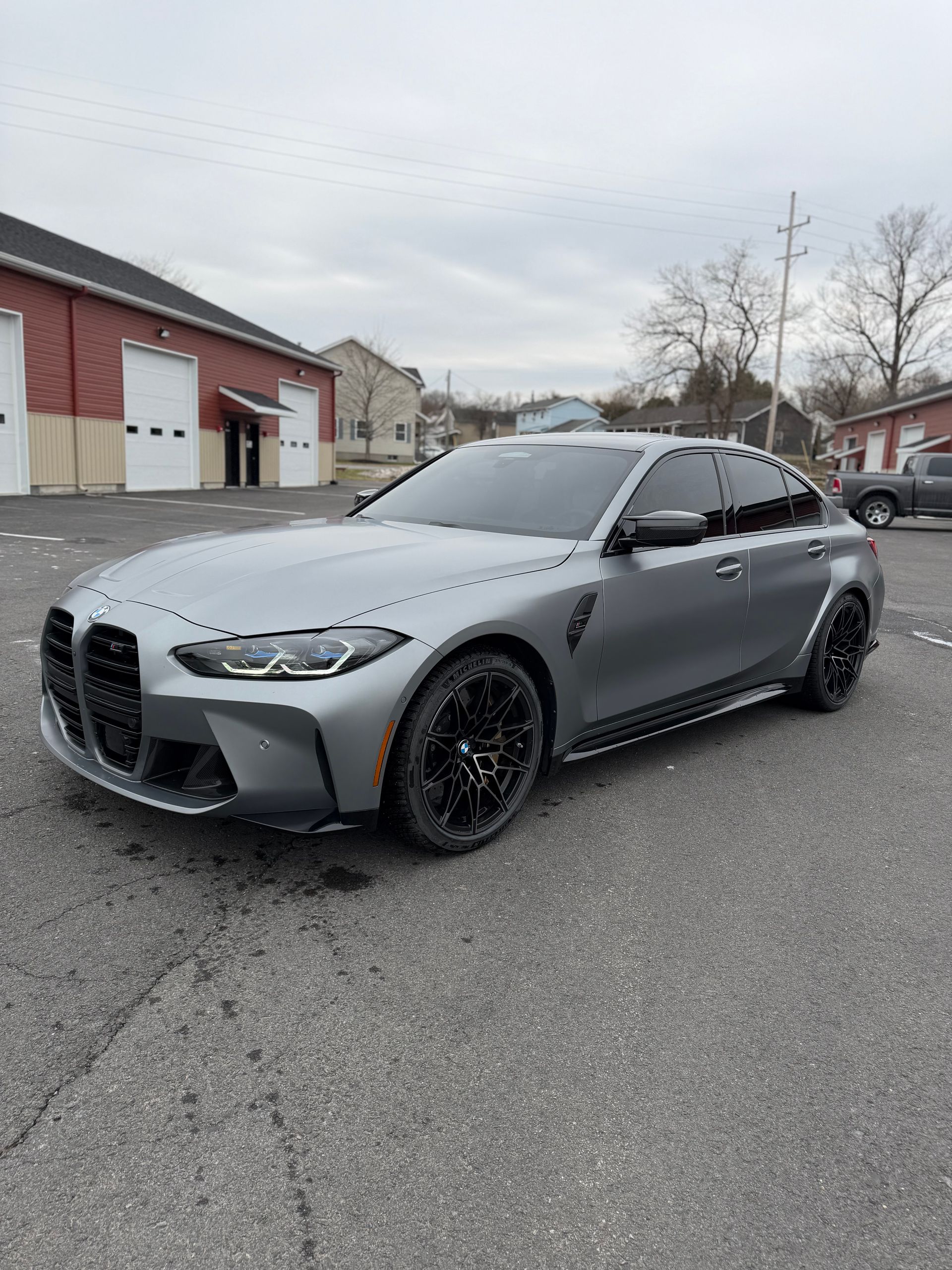 Gray BMW sedan parked on a wet street beside industrial buildings on an overcast day