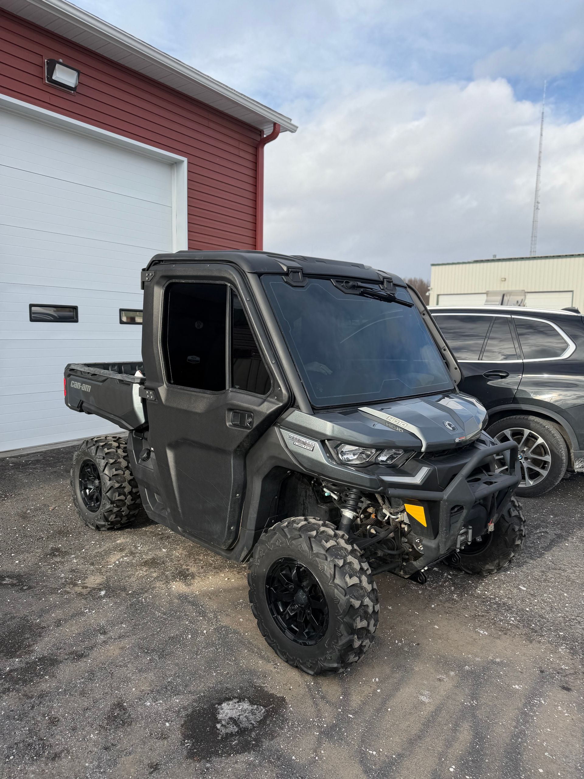 Black off-road UTV parked outside a red building beside another vehicle on gravel.