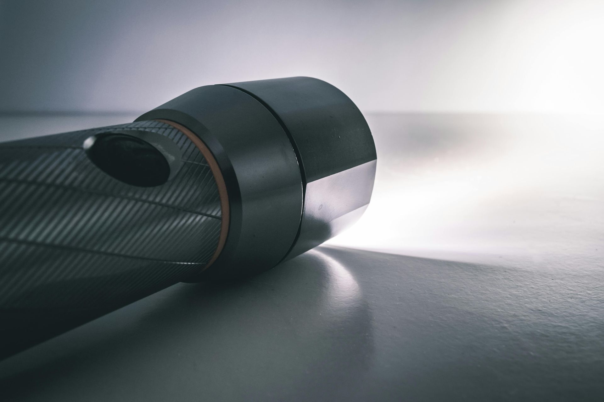 A dark, textured flashlight lying on a flat surface, casting a bright beam of light forward into crawlspace. 