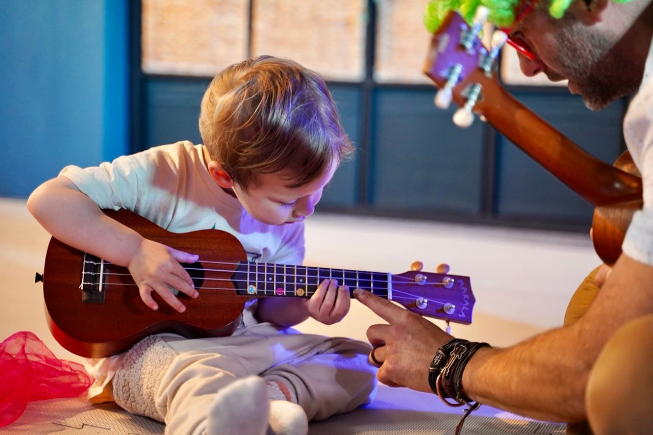 A man is teaching a young boy how to play a guitar.