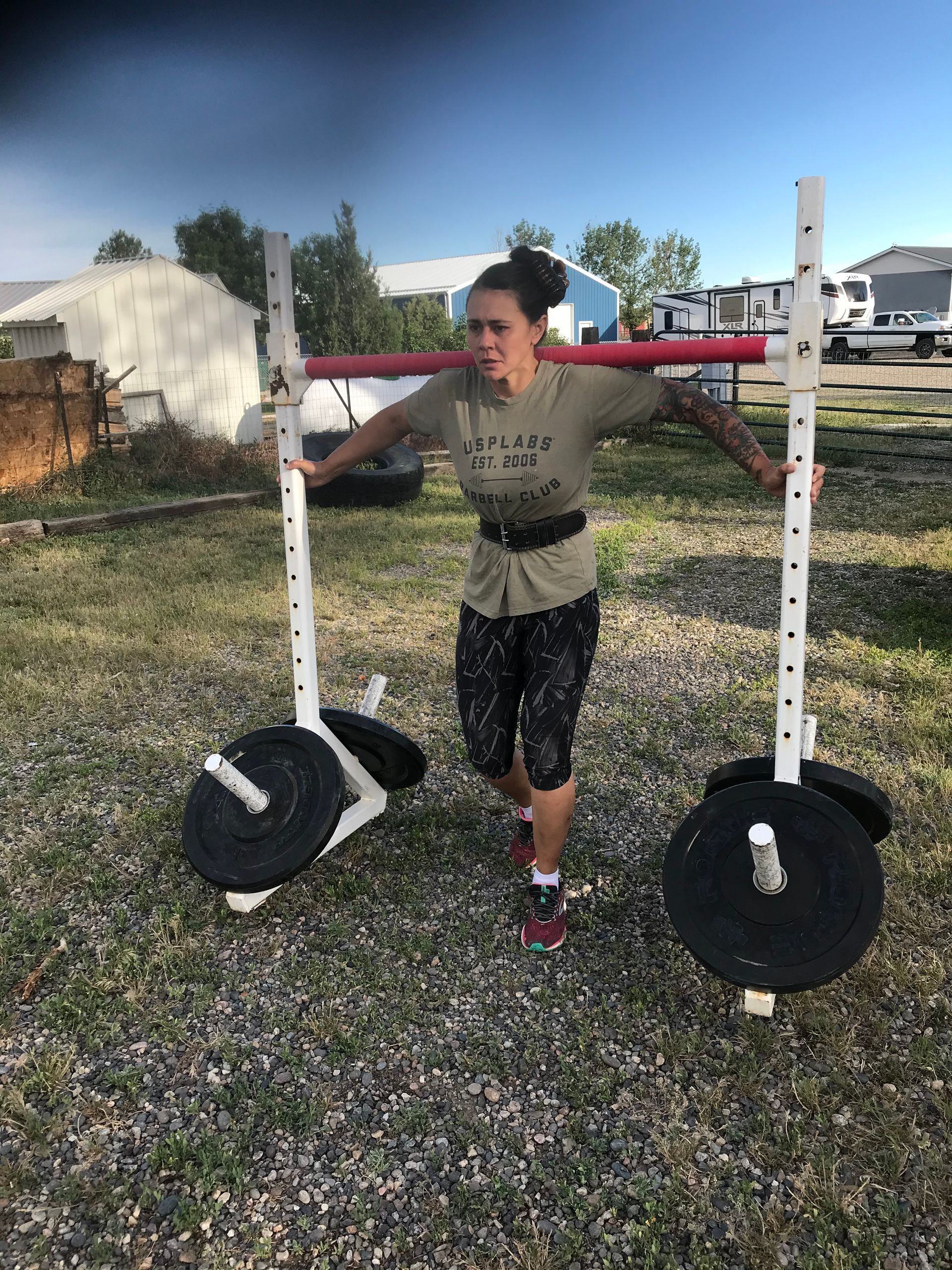 Woman lifting weights outdoors with a homemade squat rack, wearing a weightlifting belt.
