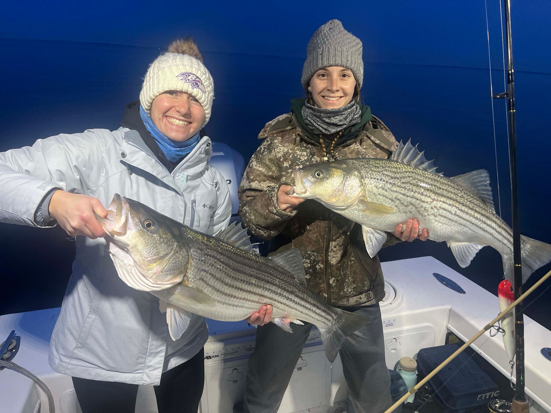 Two women are holding two large fish on a boat.