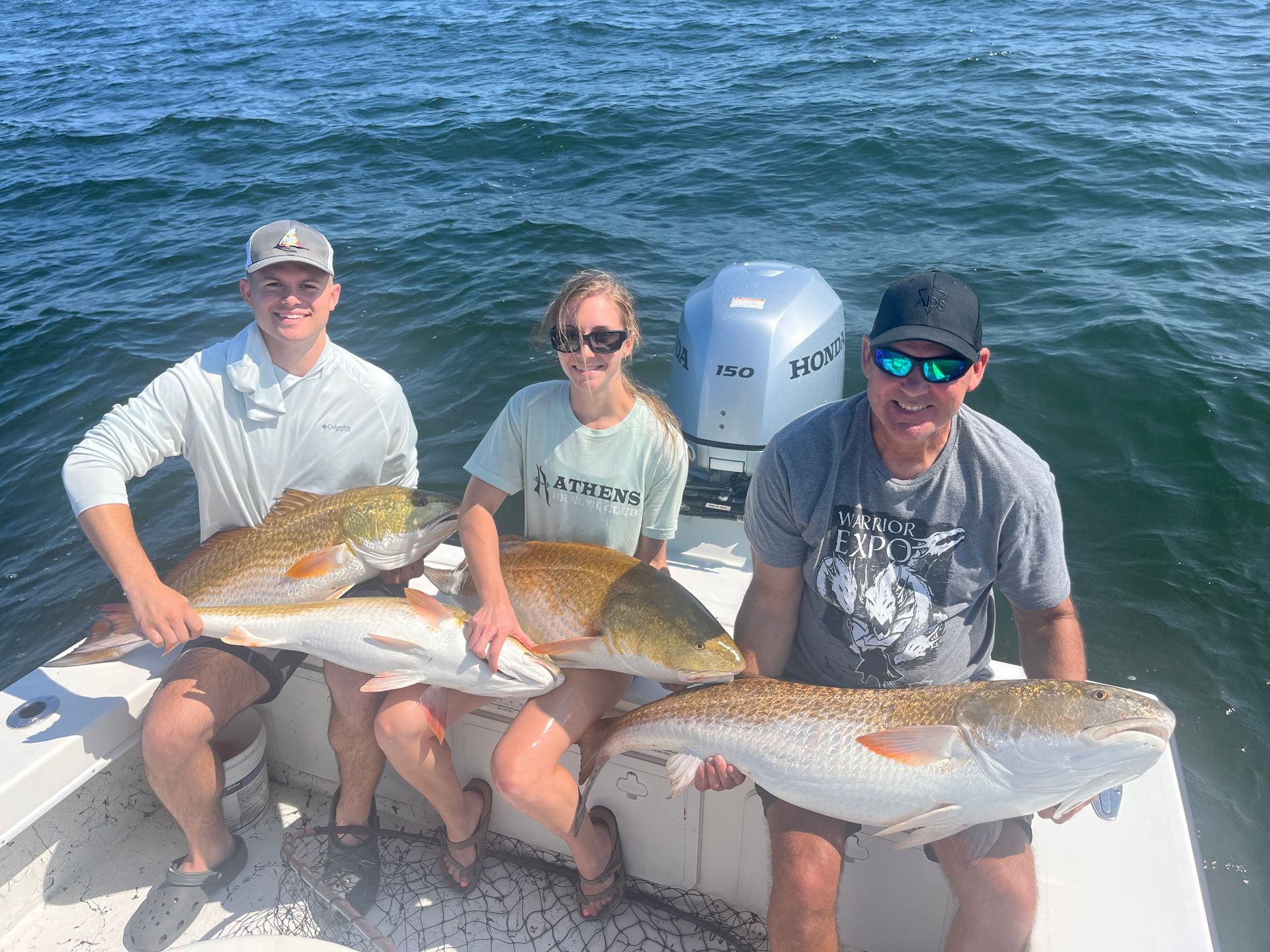 A group of people are sitting on a boat holding large fish.