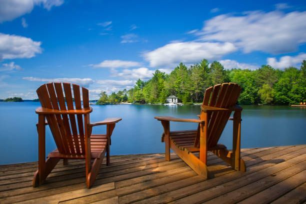 Two wooden chairs are sitting on a dock overlooking a lake.